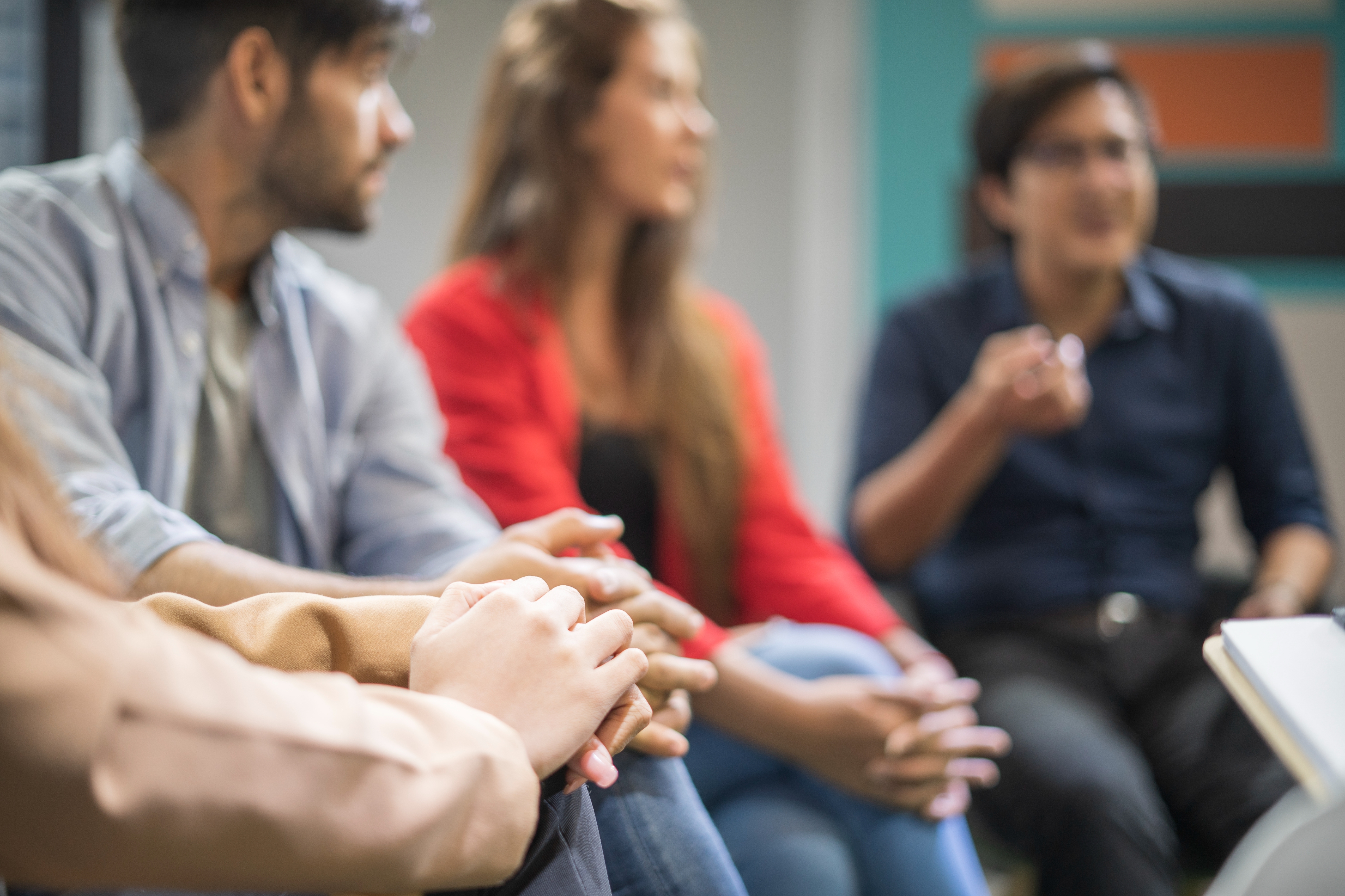 People sitting in a group discussion, focusing intently. Some gesturing while speaking. Relaxed, informal setting