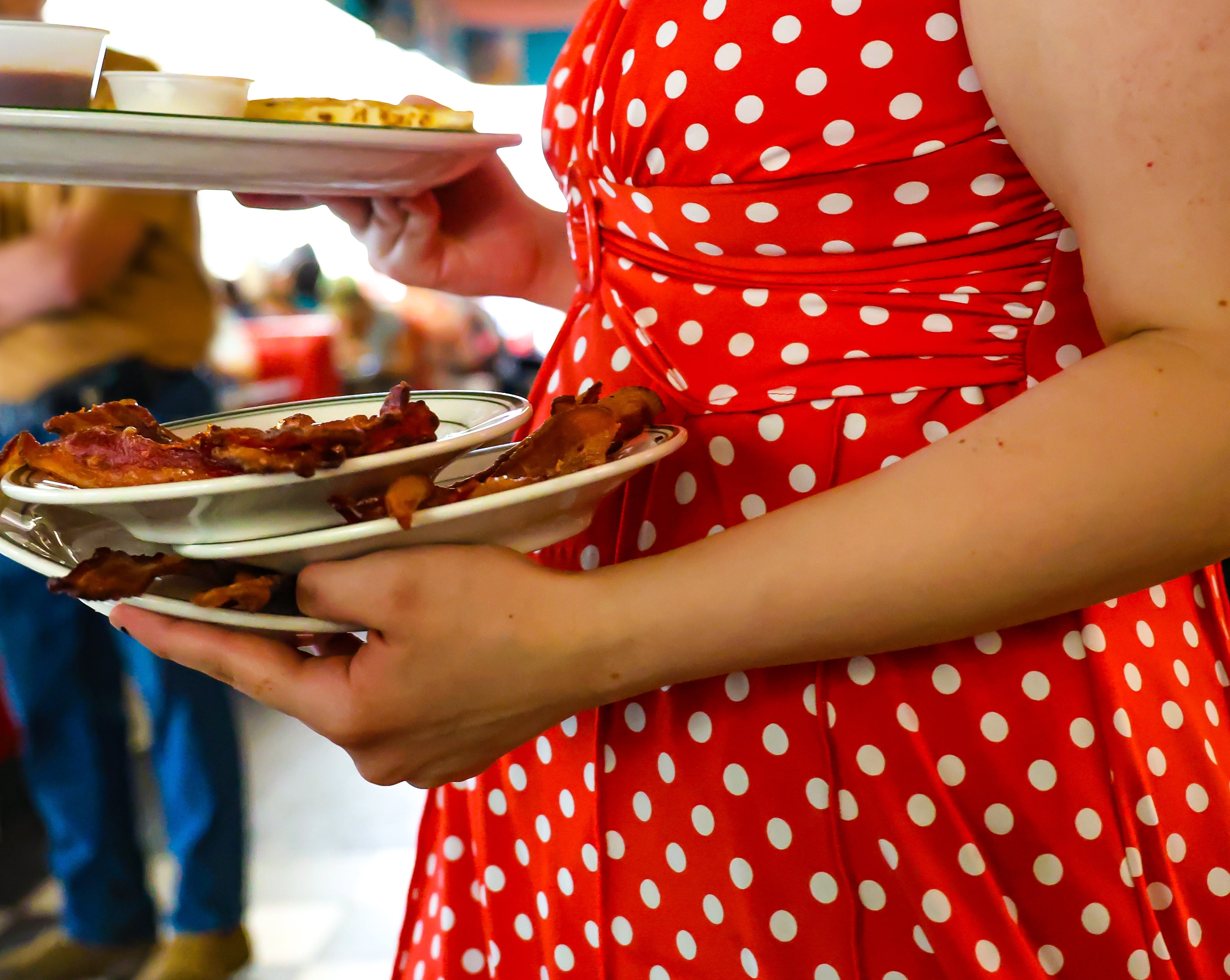 Person holding plates of food inside a busy diner. They are wearing a polka dot dress