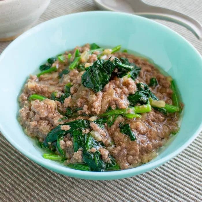 ひき肉とほうれん草が入ったスープが青いボウルに盛られている。テーブルにスプーンが置かれている。