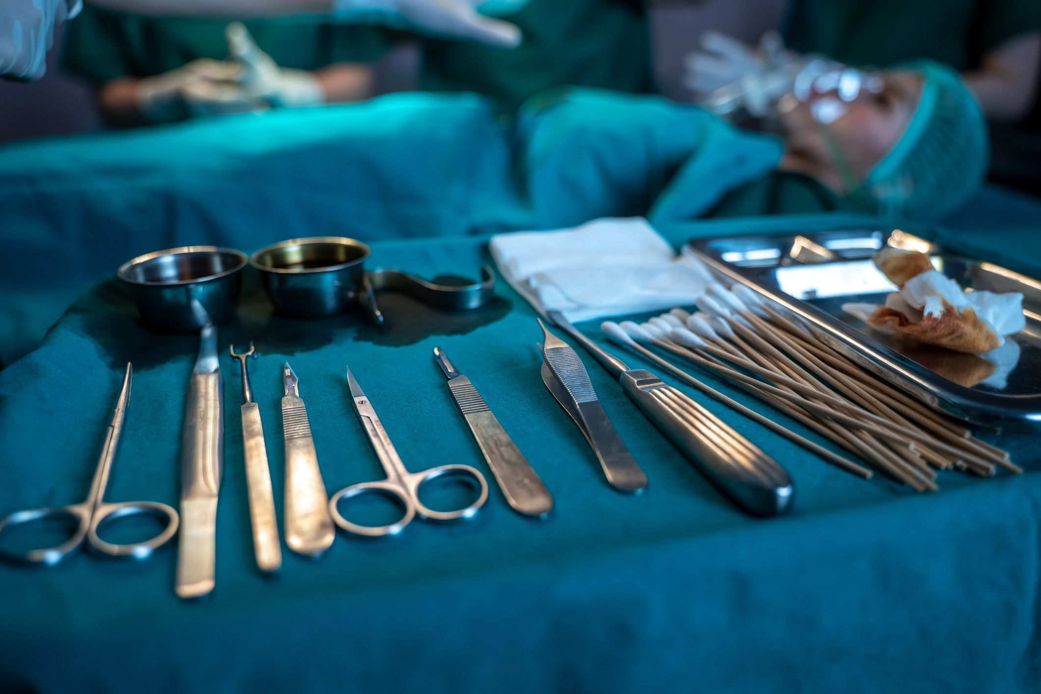 Surgical instruments neatly arranged on a table with a patient in the background undergoing a medical procedure