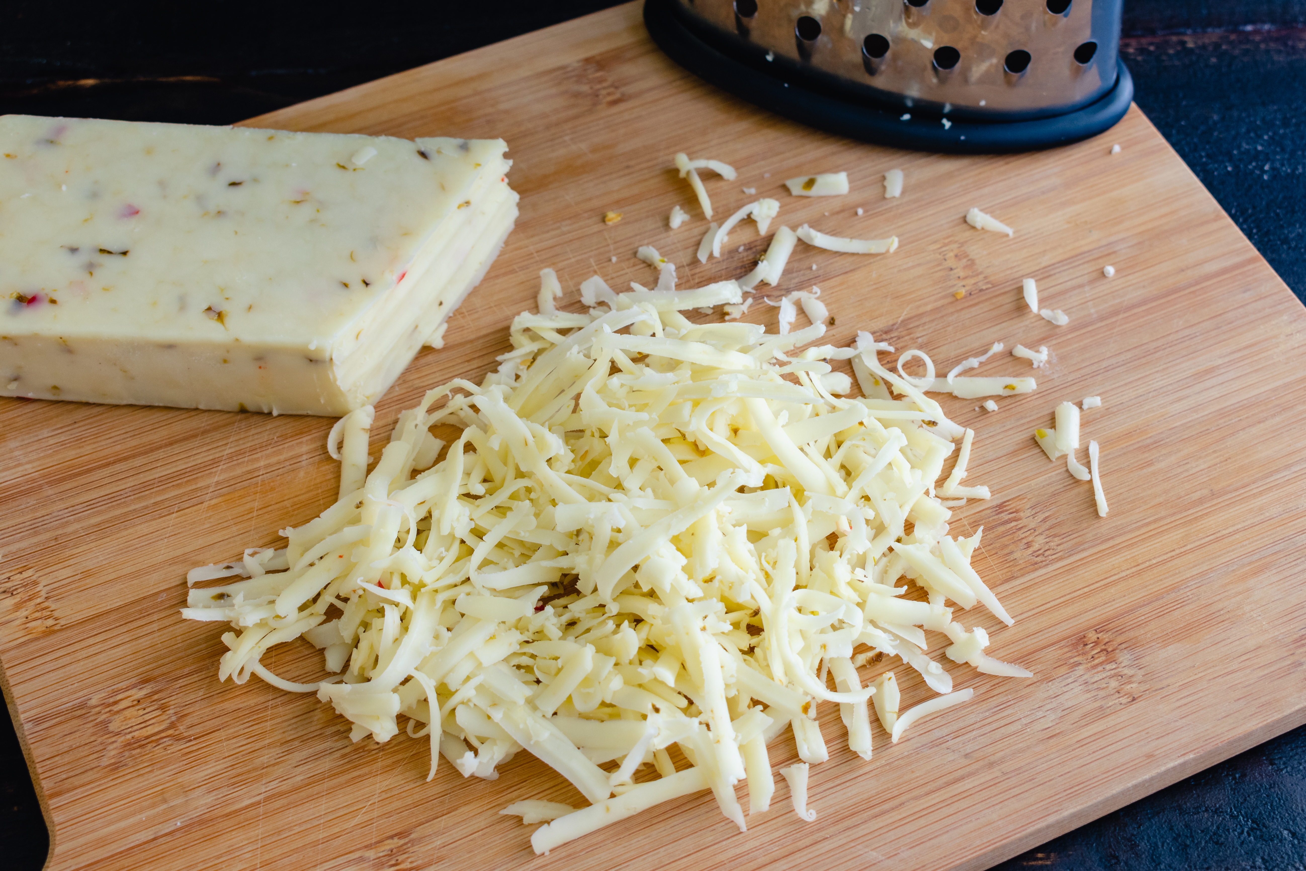 Block of cheese and grated cheese on a wooden cutting board next to a grater