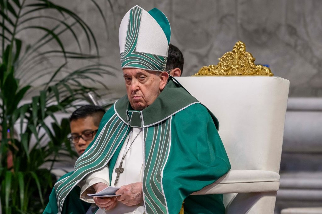 Pope Francis dressed in ceremonial religious attire sits on an ornate chair during a formal event