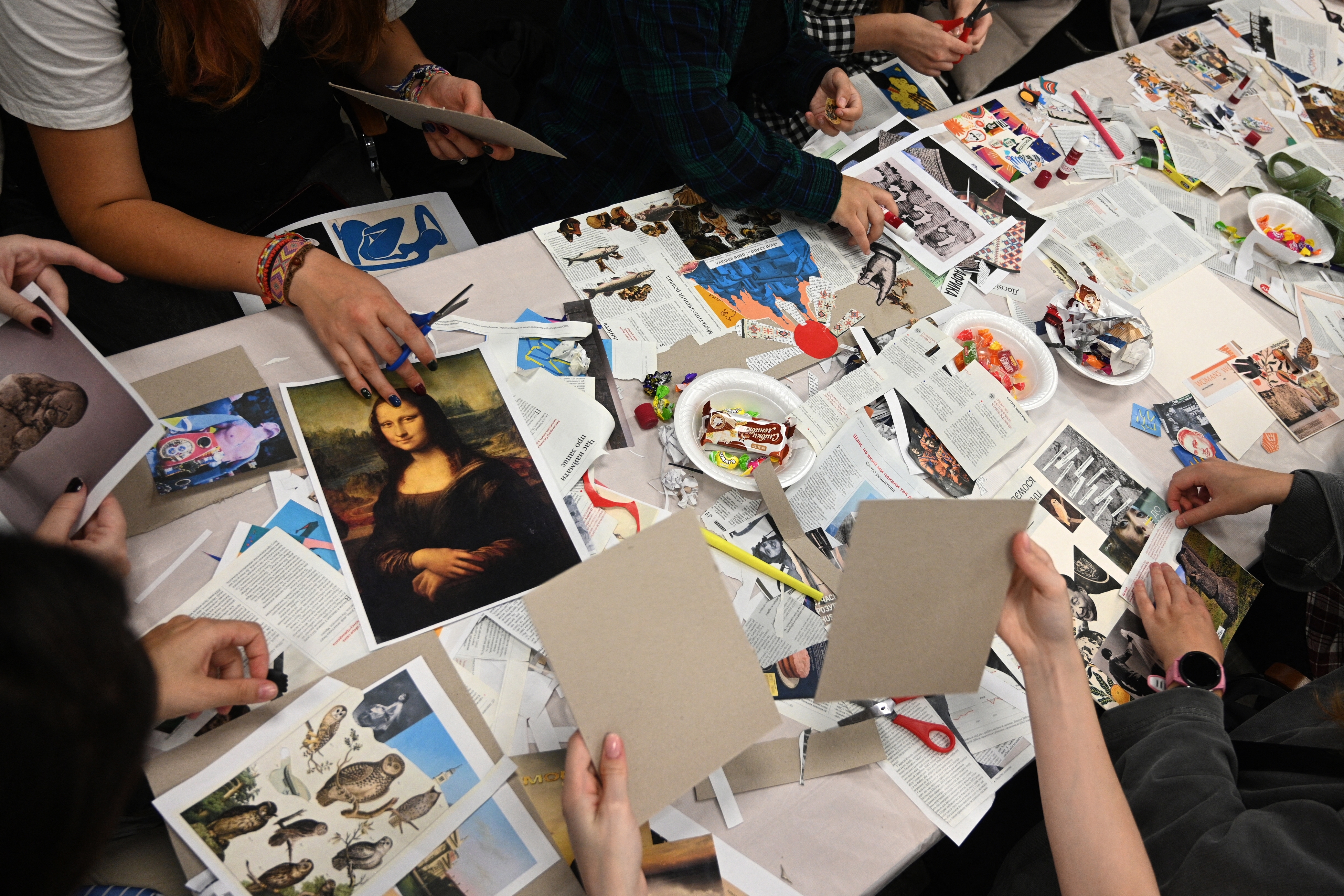 People engage in a collage-making activity at a table filled with magazine clippings, scissors, and art supplies