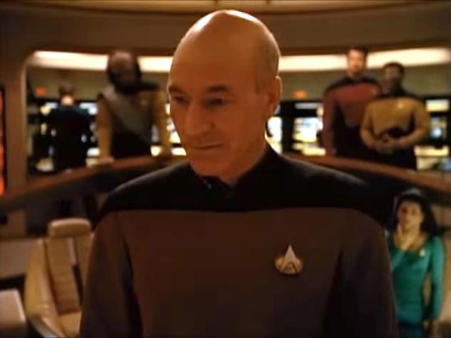 A man in a sci-fi uniform stands on a spaceship bridge surrounded by crew members