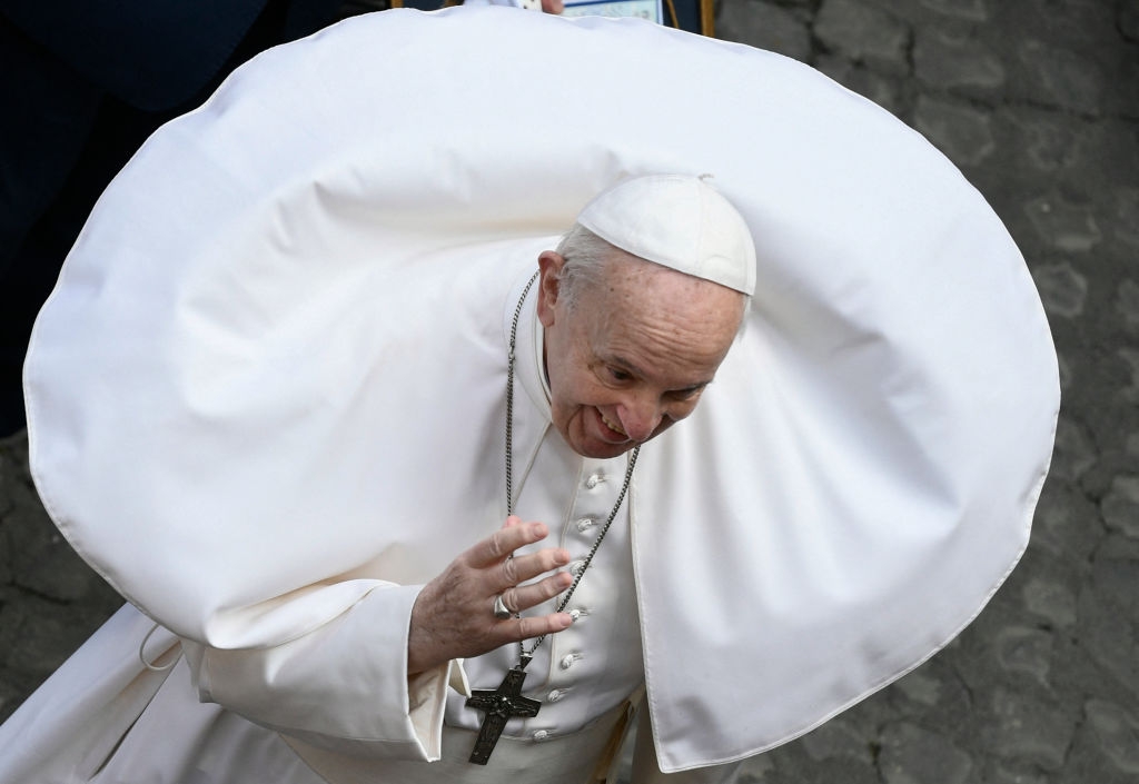 Pope Francis with wind-blown papal robes creates a humorous, dramatic swirl effect around their head, gesturing with a smile