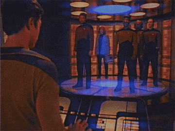 Scene of five crew members in sci-fi uniforms standing on a teleportation platform, ready to be transported, with a person operating controls