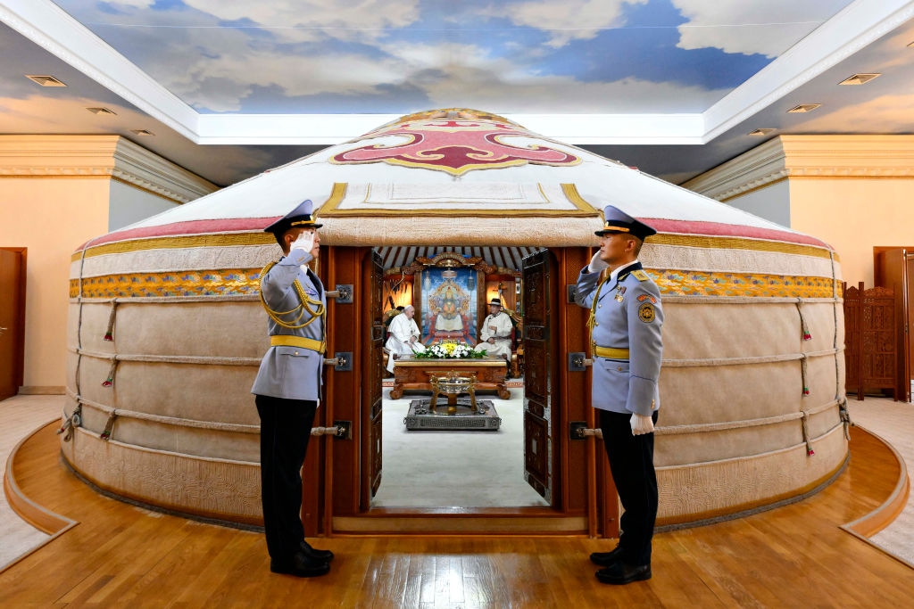 Two uniformed guards salute in front of a large, ornate yurt with an open doorway. Inside, pope francis and Khurelsukh Ukhnaa are visible near an altar-like setup
