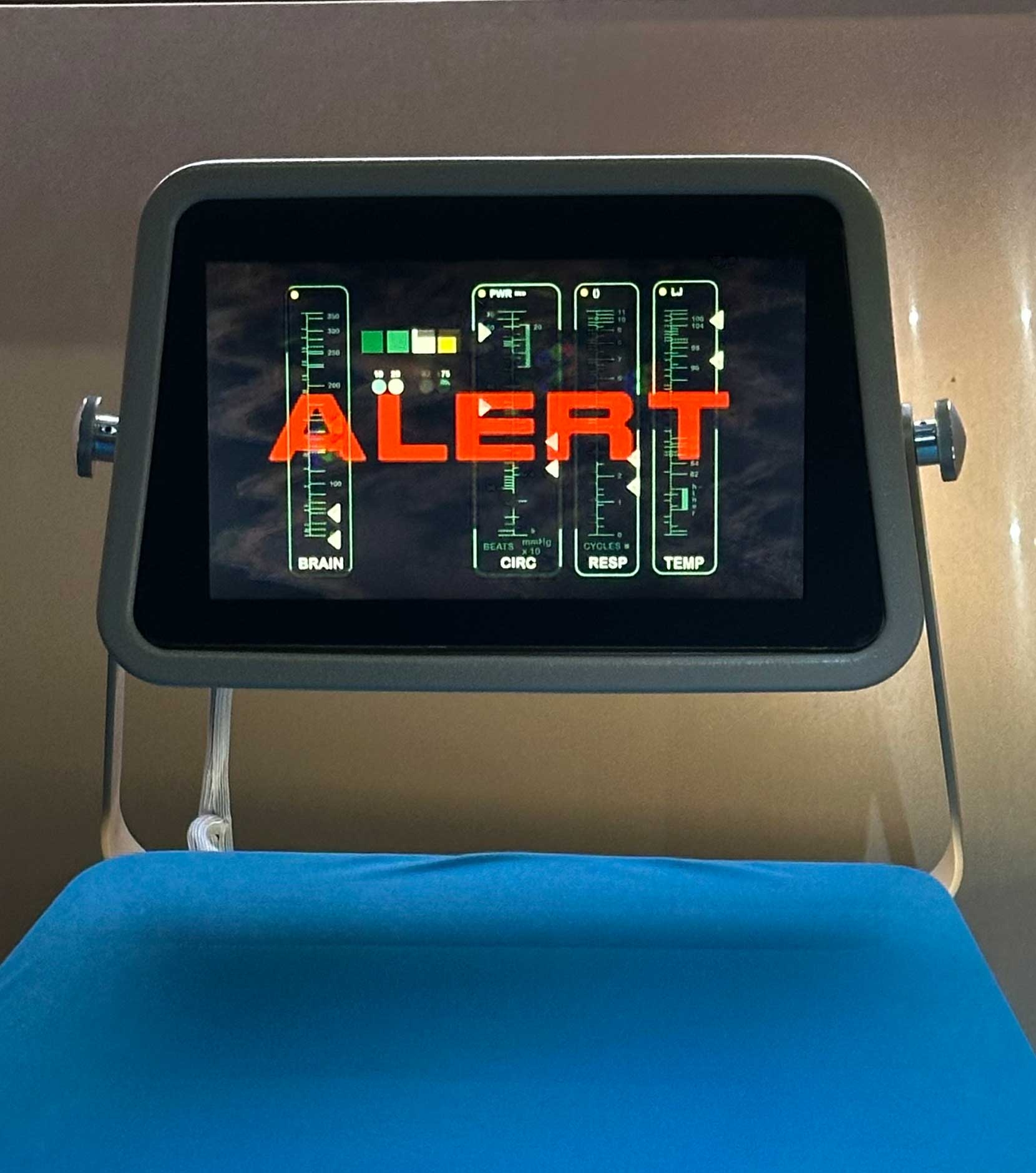 Monitor displaying "ALERT" with digital gauges for brain, cardiac, respiratory, and temperature readings