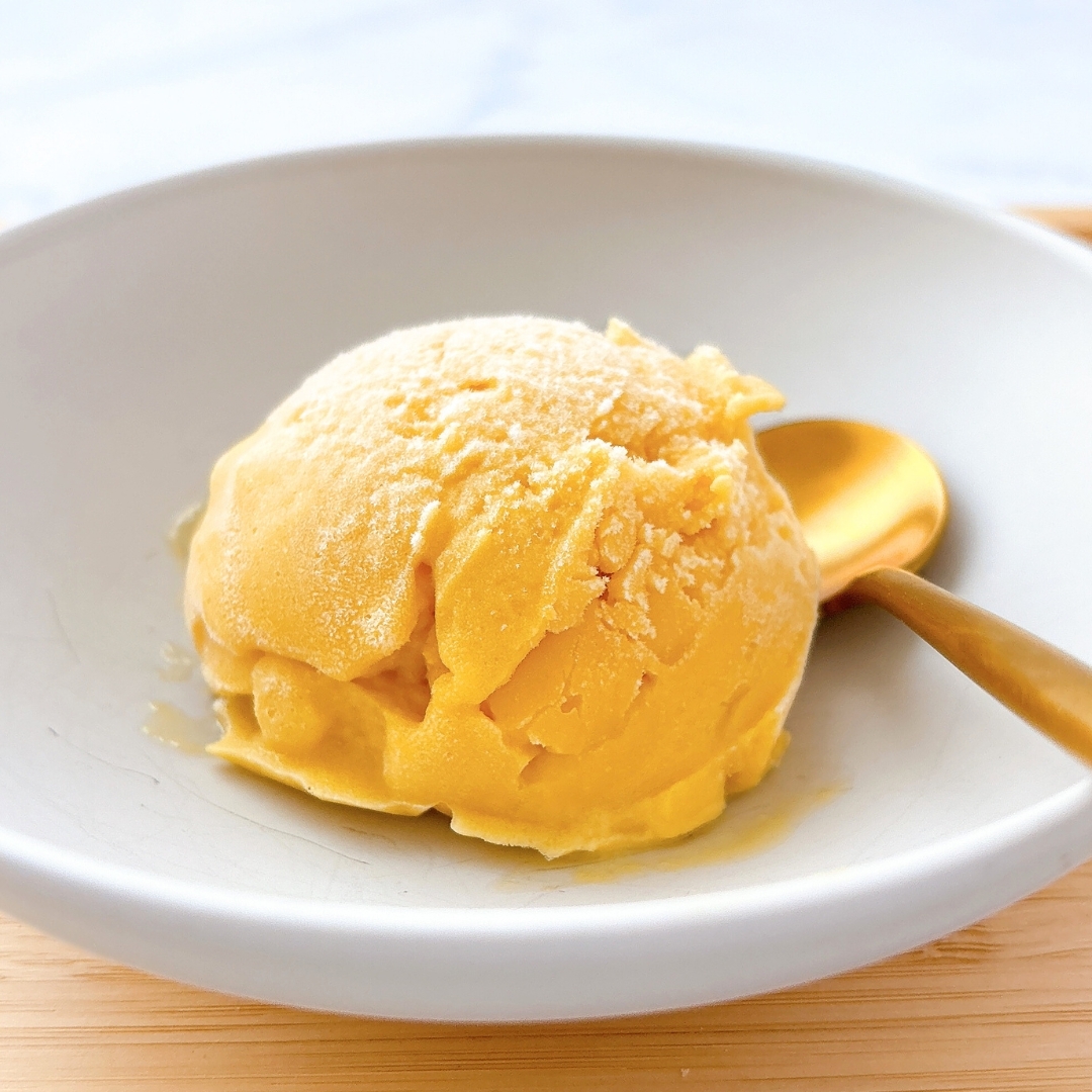 白い皿に乗ったアイスクリームのスクープと金色のスプーン。