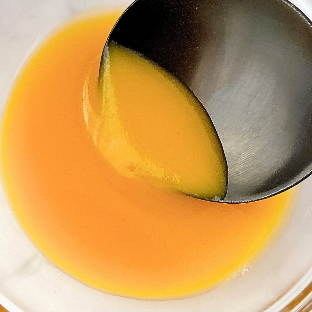 金属のスプーンでオレンジ色のソースがボウルに注がれている。