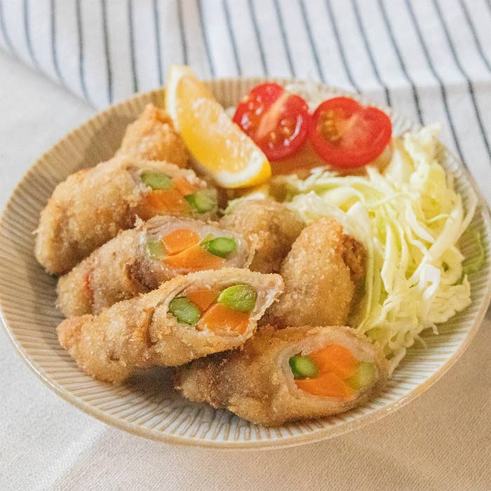 揚げ物の盛り合わせ。アスパラとニンジンの肉巻きフライが皿に盛られ、付け合わせにキャベツ、プチトマト、レモンが添えられている。