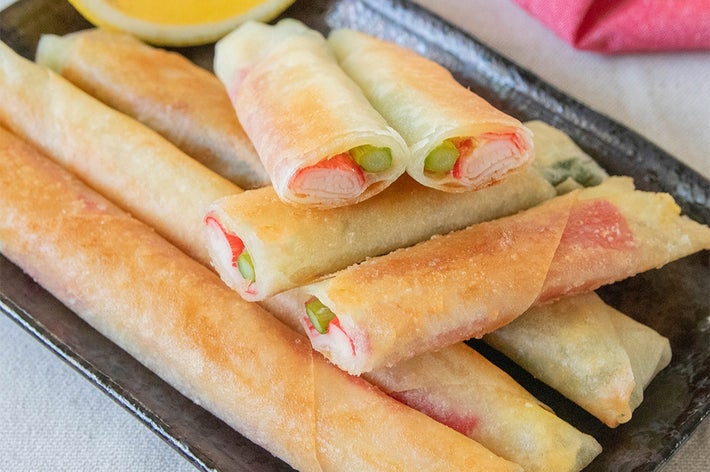 黒い皿に盛られたアスパラとカニカマの春巻きと、レモンスライス。