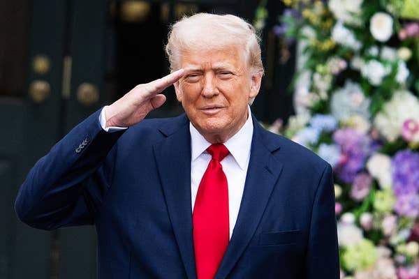 A person in a suit and red tie is saluting in front of floral arrangements