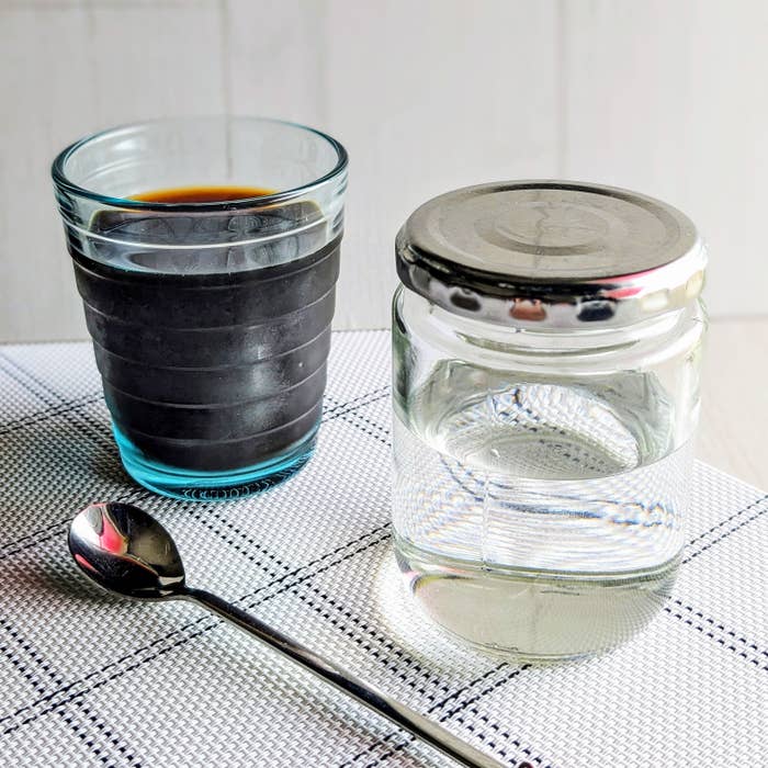 コーヒーの入ったグラスと水の入った蓋付きジャー、スプーンが布製のランチョンマットの上に置かれている。