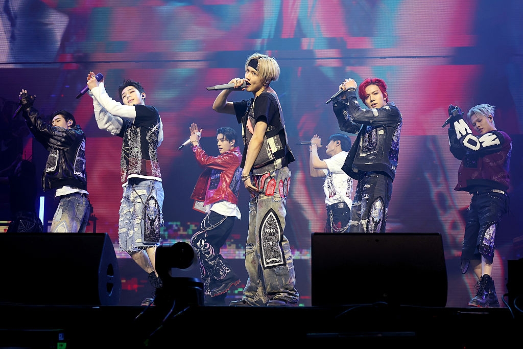 Group of male performers on stage in energetic poses, wearing styled denim and leather outfits