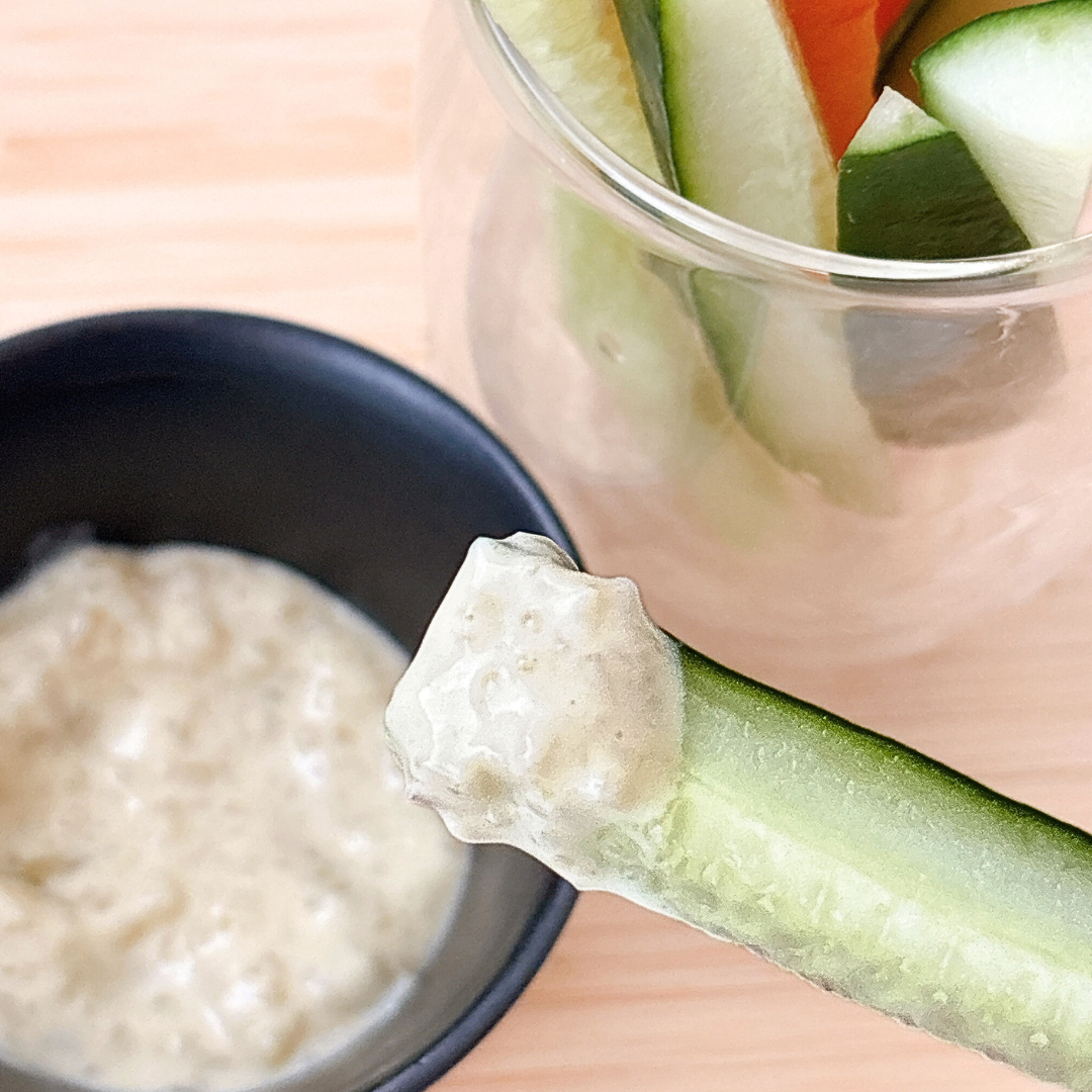 キュウリスティックがディップソースに浸され、ガラス容器に他の野菜が入っている状態が見える。