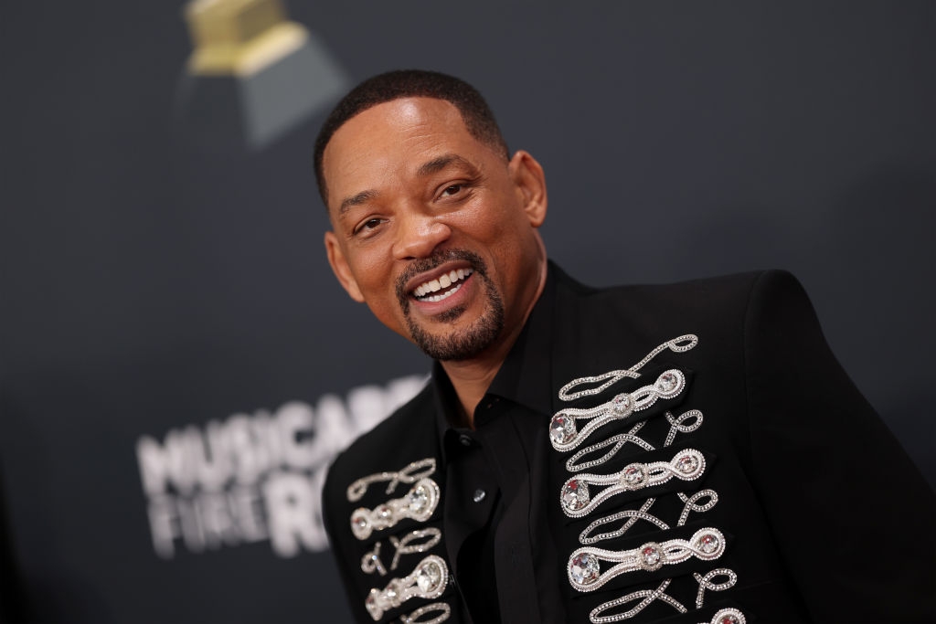 Man in embellished jacket on red carpet, smiling at event