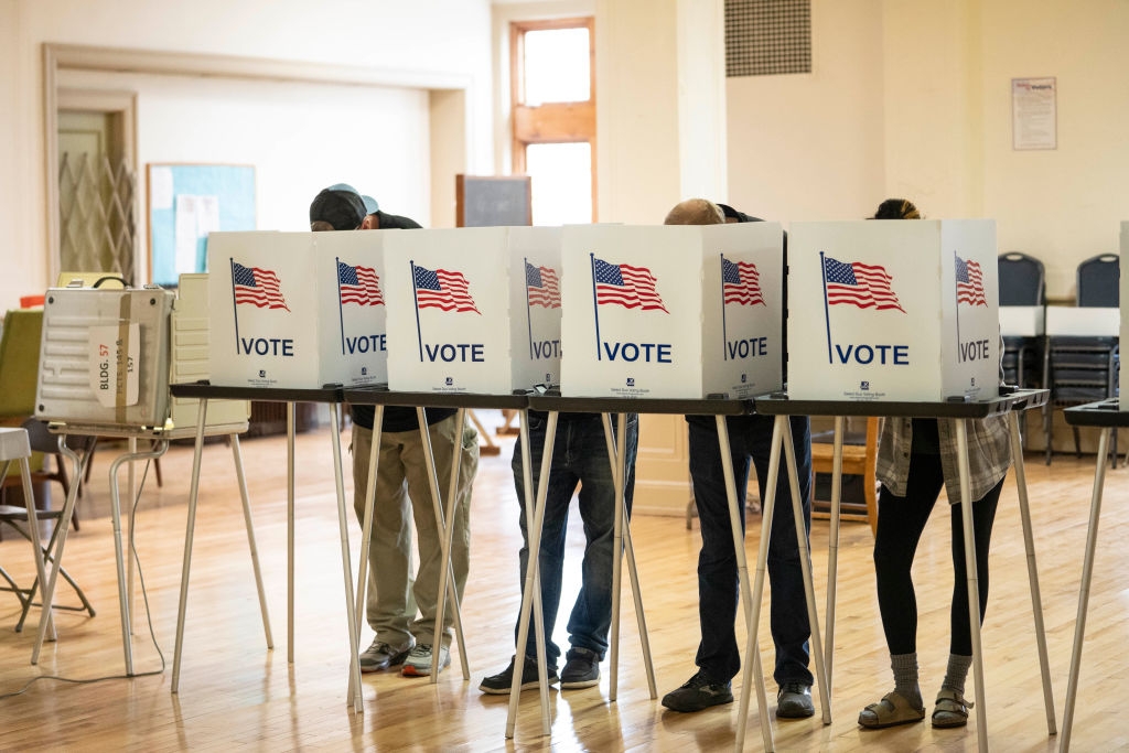 People casting votes in privacy booths at a polling station with &quot;I VOTE&quot; signs visible