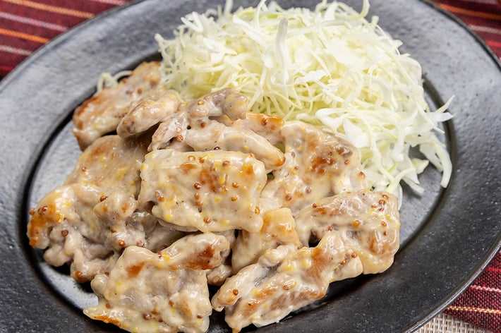 黒い皿に載ったマヨネーズと粒マスタードがからんだ豚こま肉の料理と千切りキャベツ。