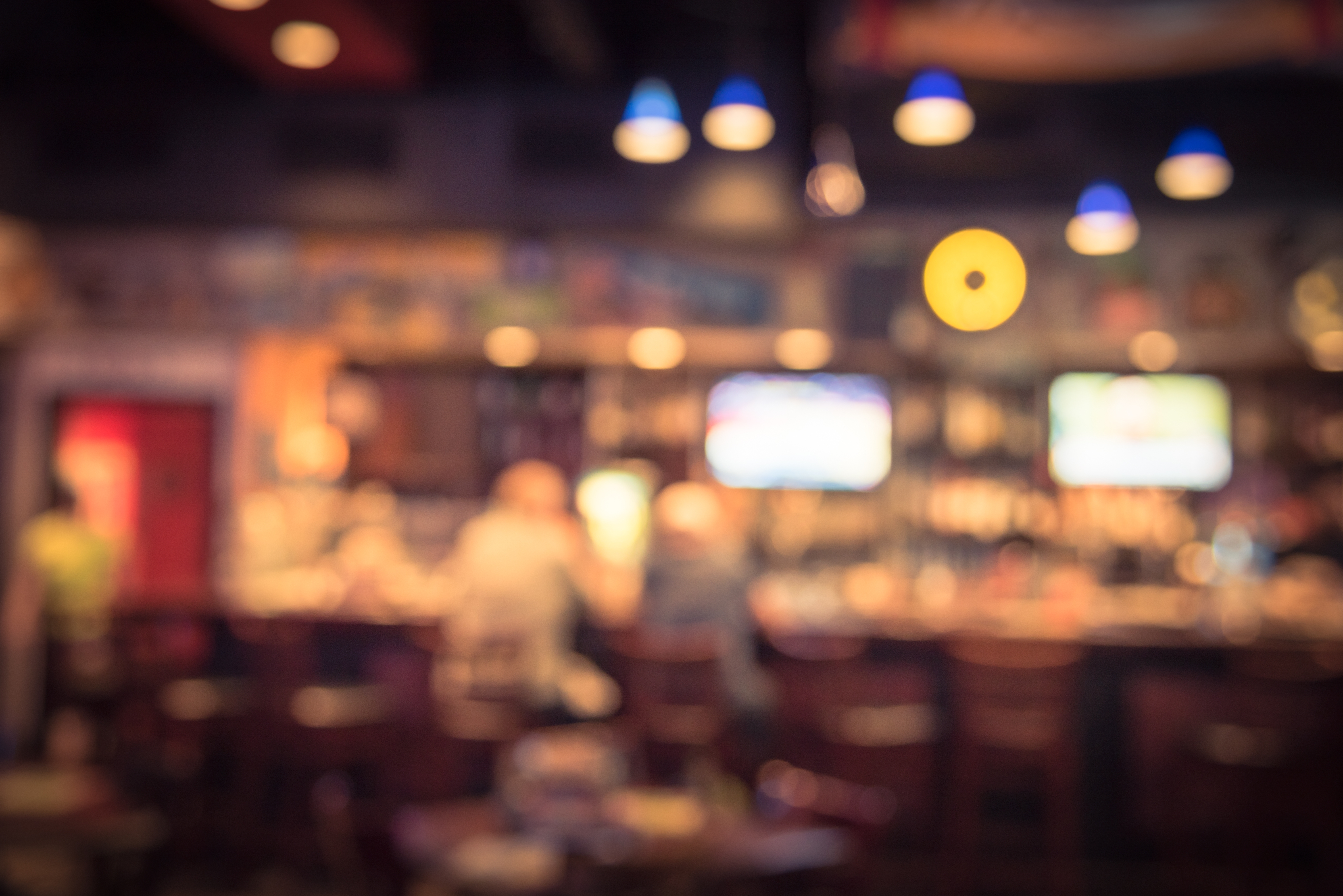 Blurred image of a bar interior with patrons at the counter and soft lighting, creating a cozy, relaxed atmosphere