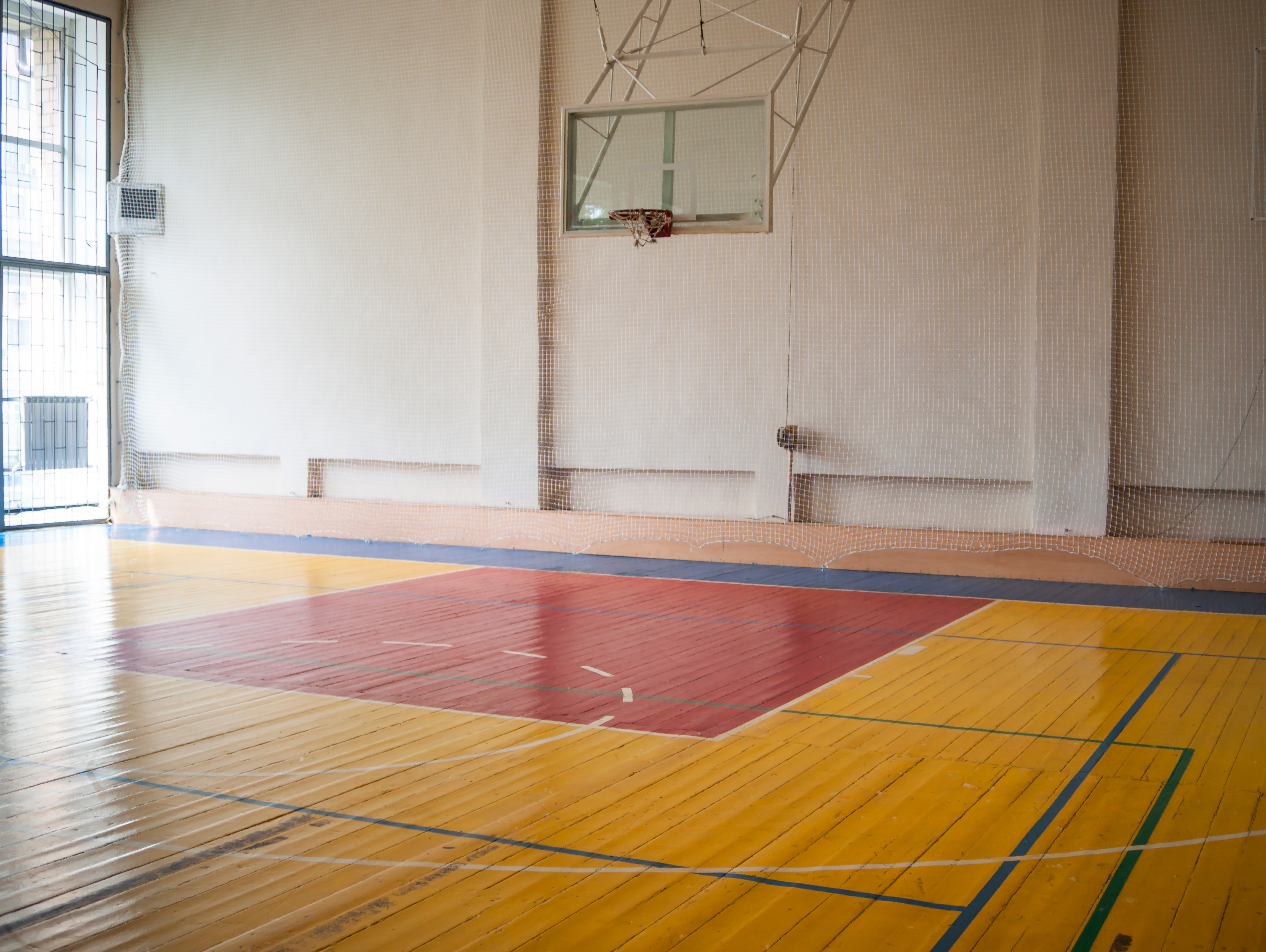 Empty indoor basketball court with hardwood flooring and a hoop
