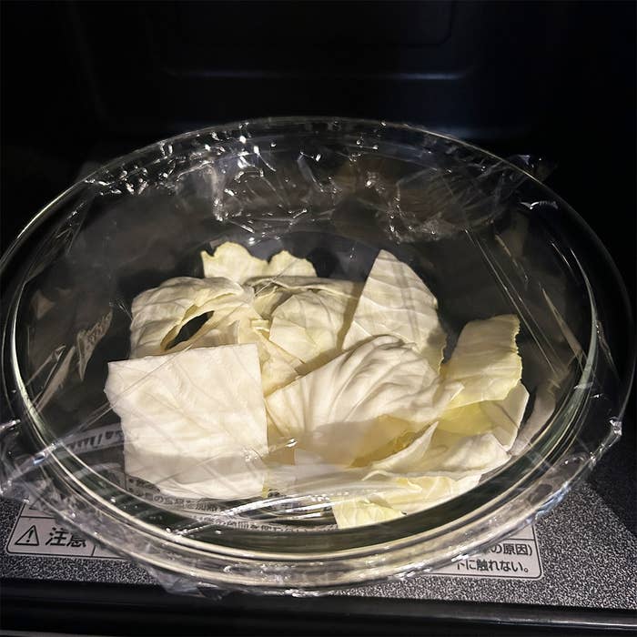 電子レンジの中でラップをかけたガラスボウルにキャベツの葉。注意書きあり。