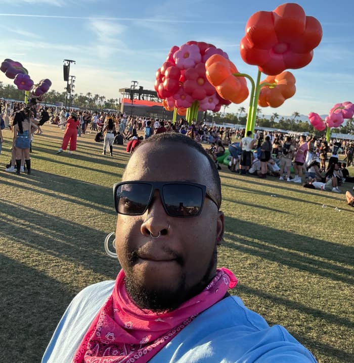 Person in sunglasses taking a selfie at a music festival with colorful balloon sculptures in the background