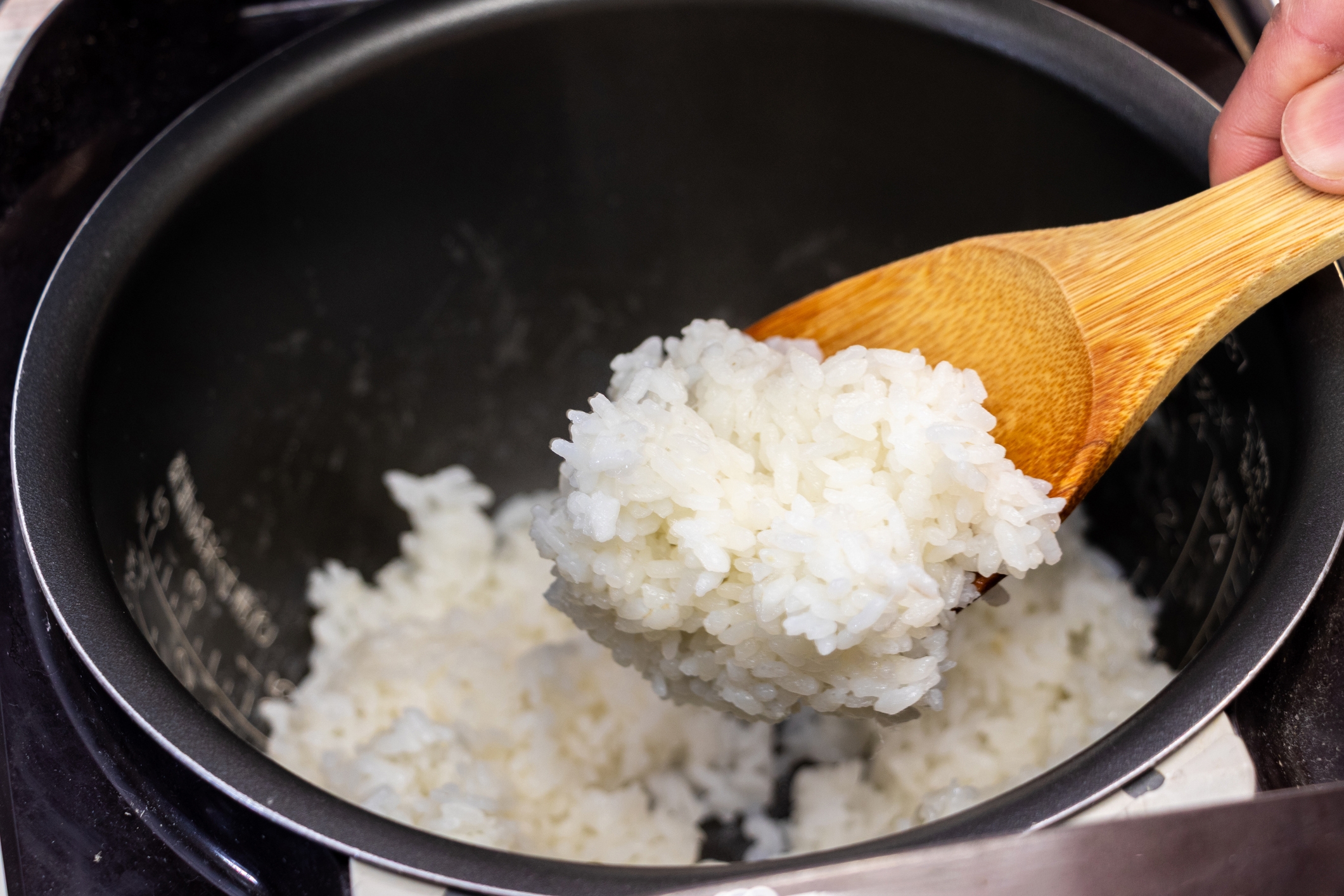 Cooked rice being scooped from a rice cooker with a wooden spoon