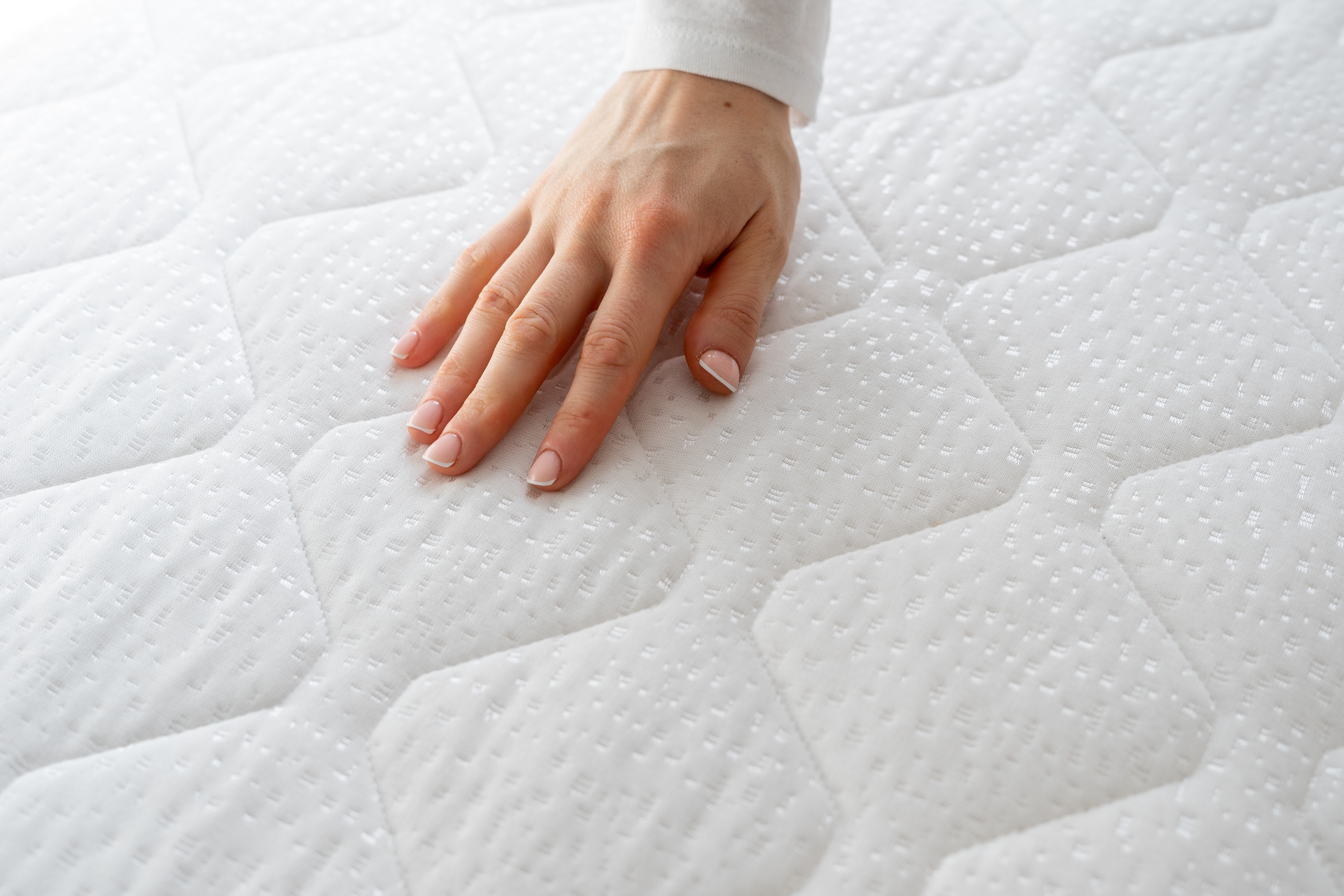 A hand gently presses down on a quilted mattress surface, showcasing its texture and softness