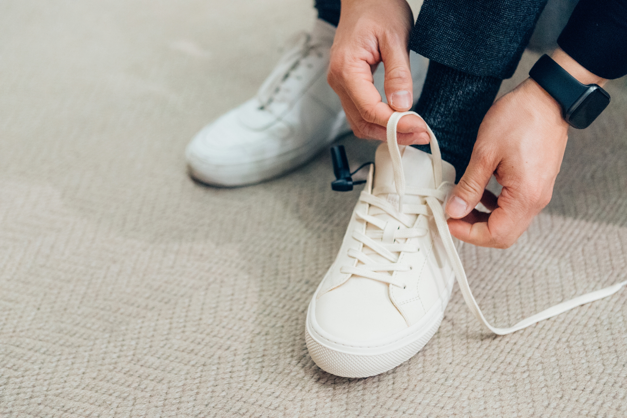 Person tying shoelaces on casual sneakers while wearing a smartwatch