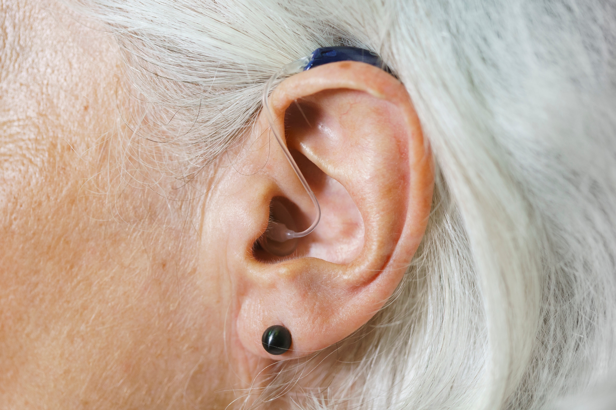 A close-up of an elderly person's ear wearing a hearing aid, illustrating assistive technology use
