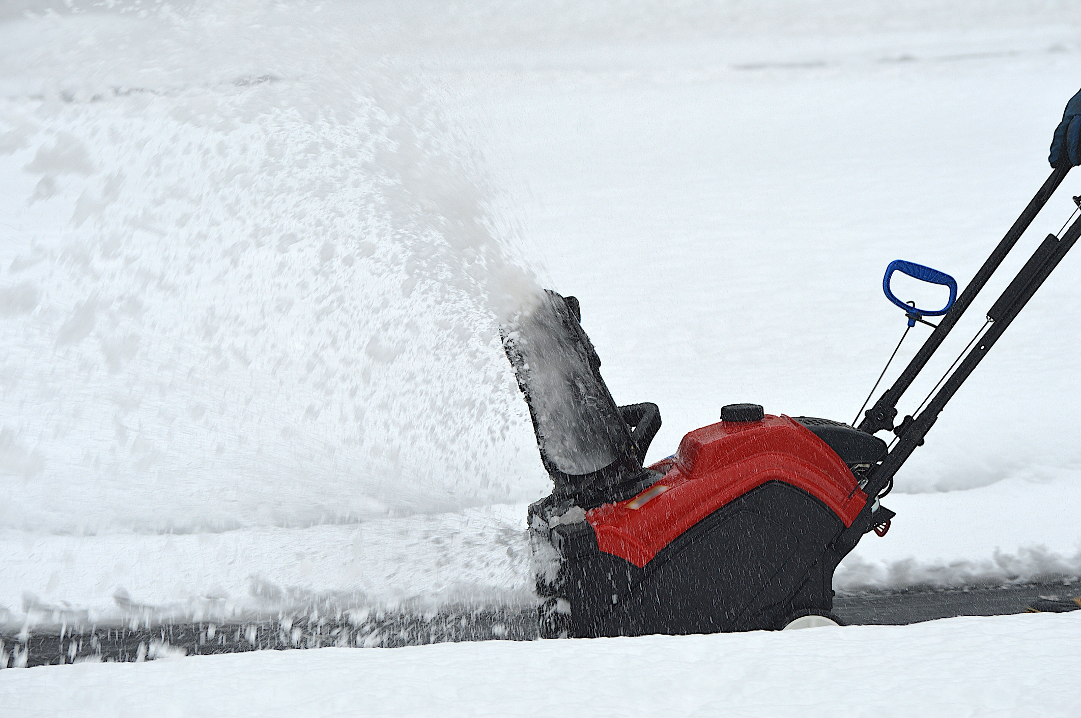Person using snow blower to clear driveway in snowy weather