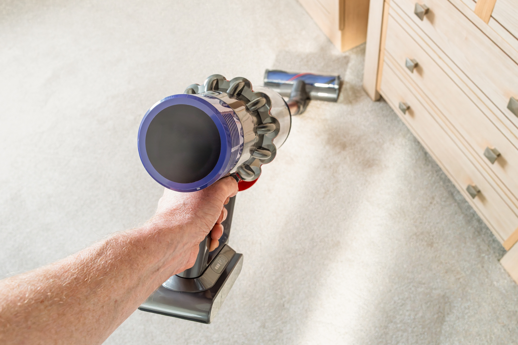 Person vacuuming a carpet near a dresser with a cordless vacuum cleaner