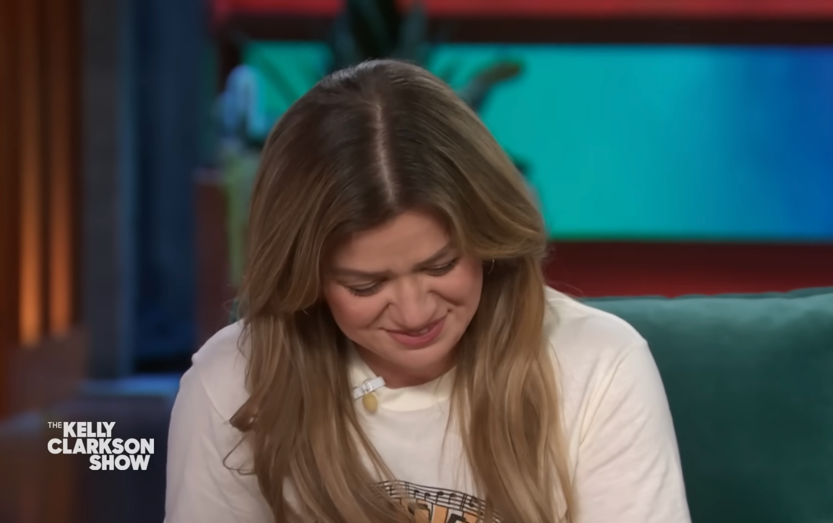 Kelly Clarkson smiling and looking down on a talk show