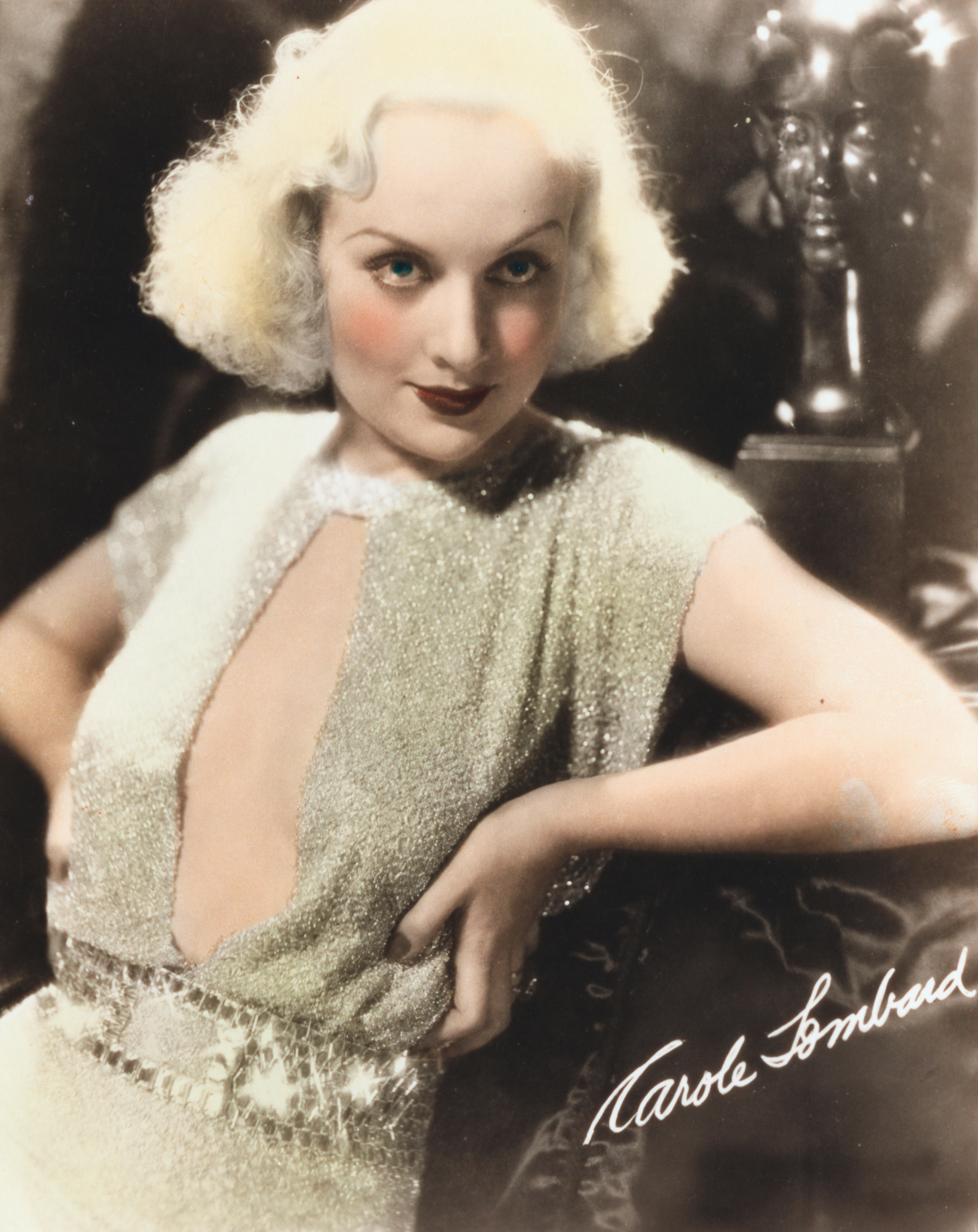 Person in vintage glam dress with short, wavy hair poses leaning on a chair indoors