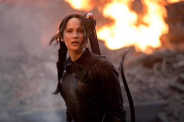 Katniss in a scene from Mockingjay, where she looks concerned as fire blazes behind her