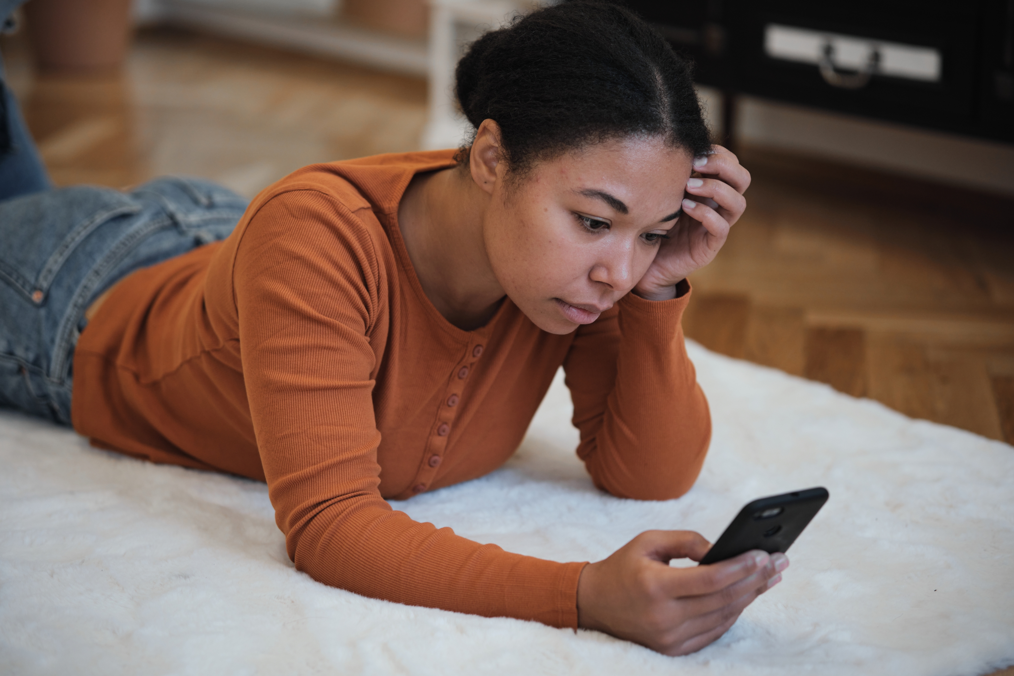 Woman lying on the ground with one hand holding her phone and the other hand on her head