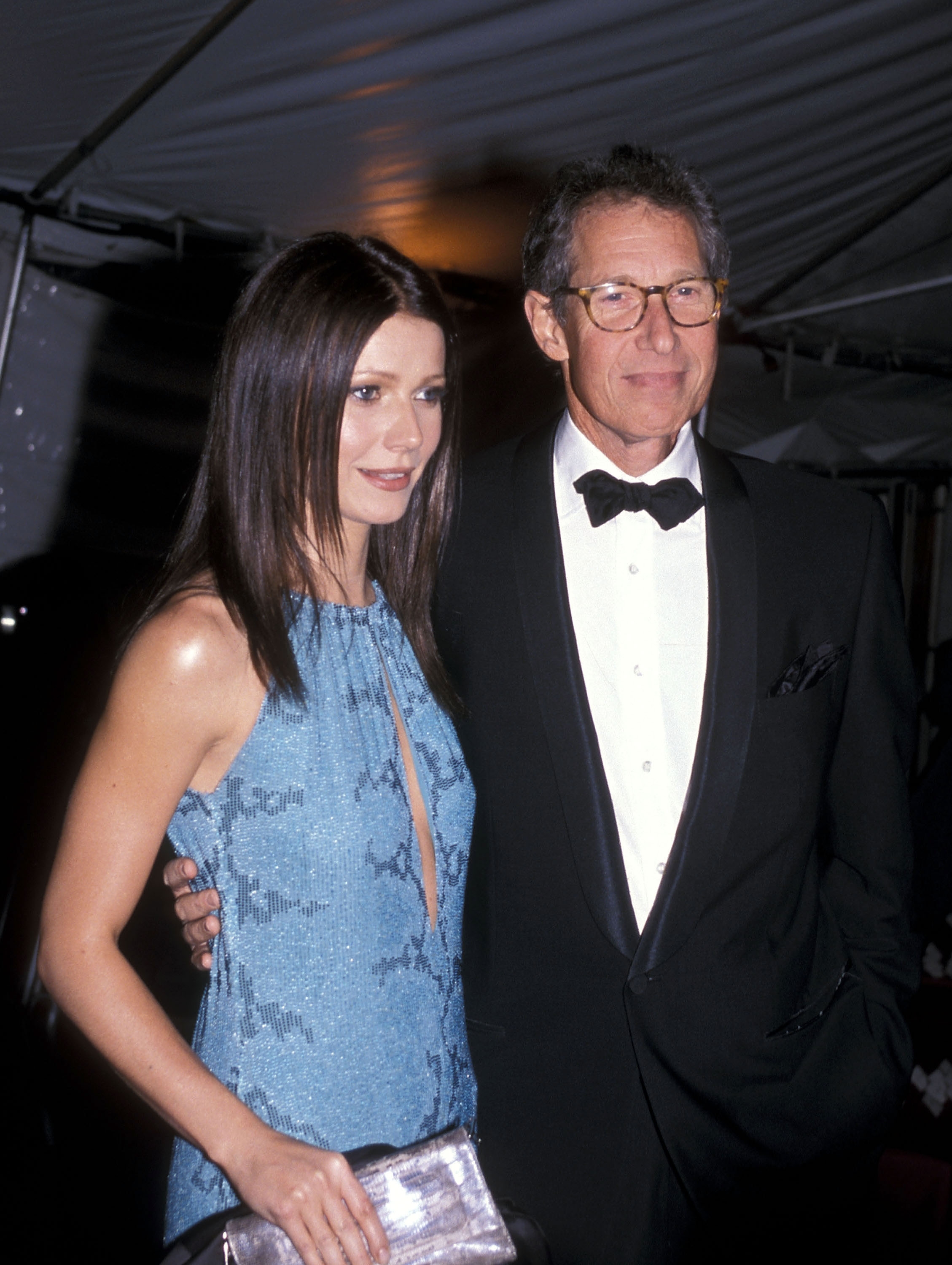 A man in a tuxedo and a woman in a stylish sleeveless evening gown pose together at a formal event