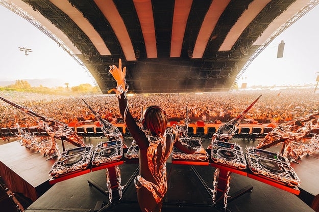 DJ performing at a large outdoor music festival with a massive crowd under a spacious canopy