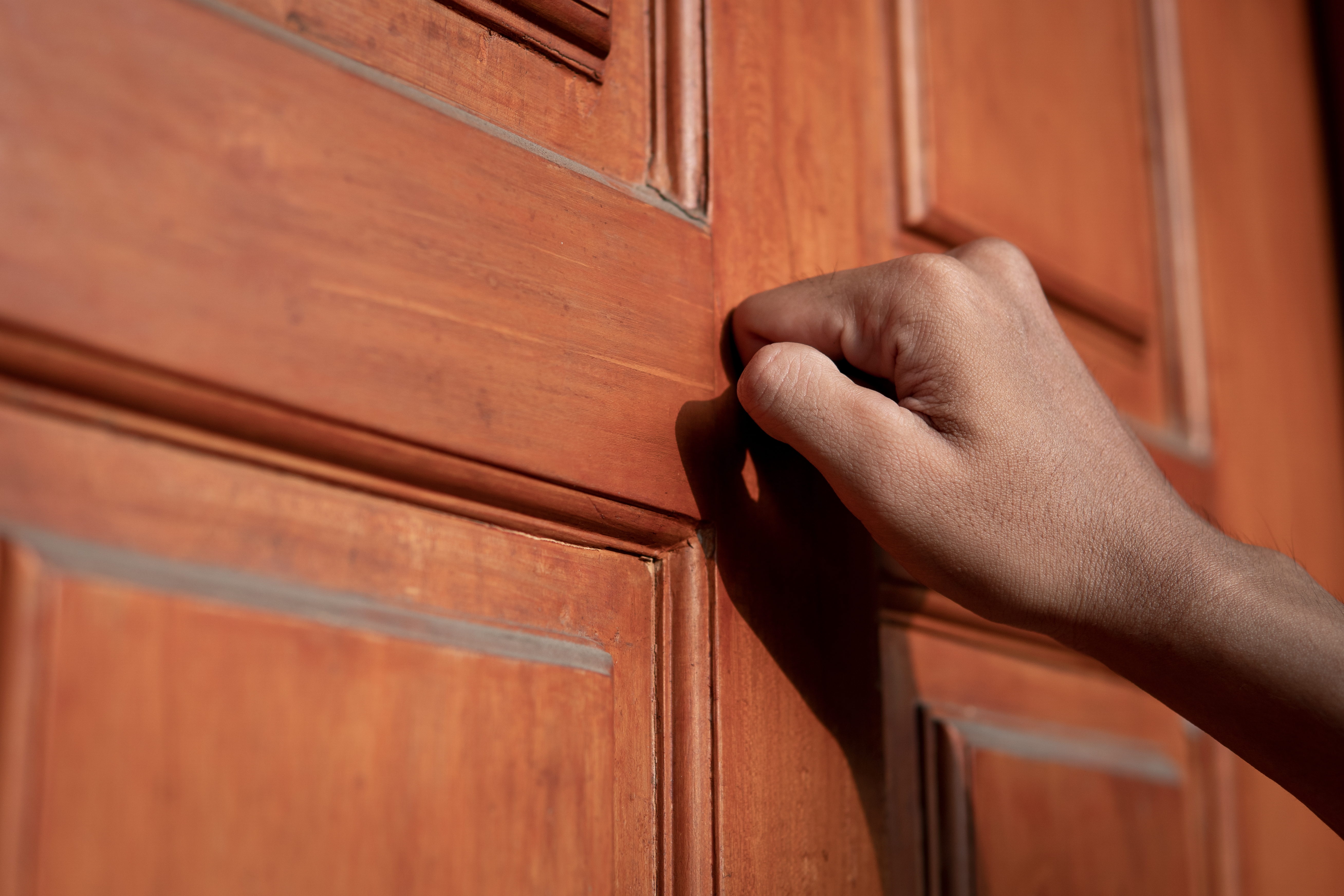 Hand knocking on a wooden door, suggesting anticipation or the arrival of news