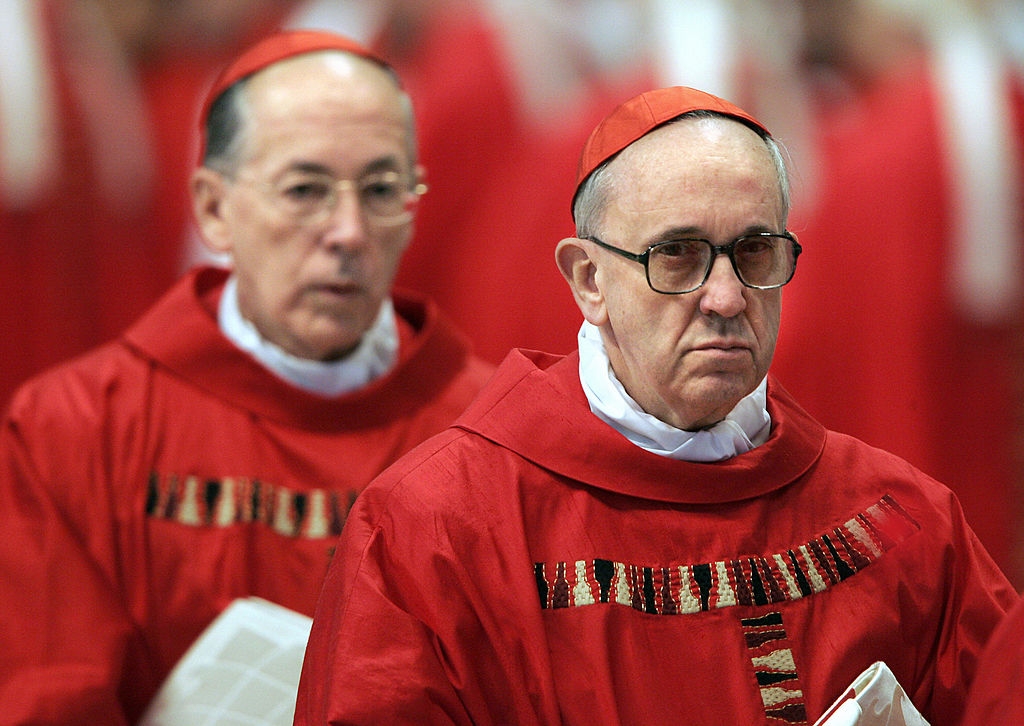 Cardinal Bergoglio, in front of another Cardinal in formal red robes and hats, walks in procession during a religious ceremony
