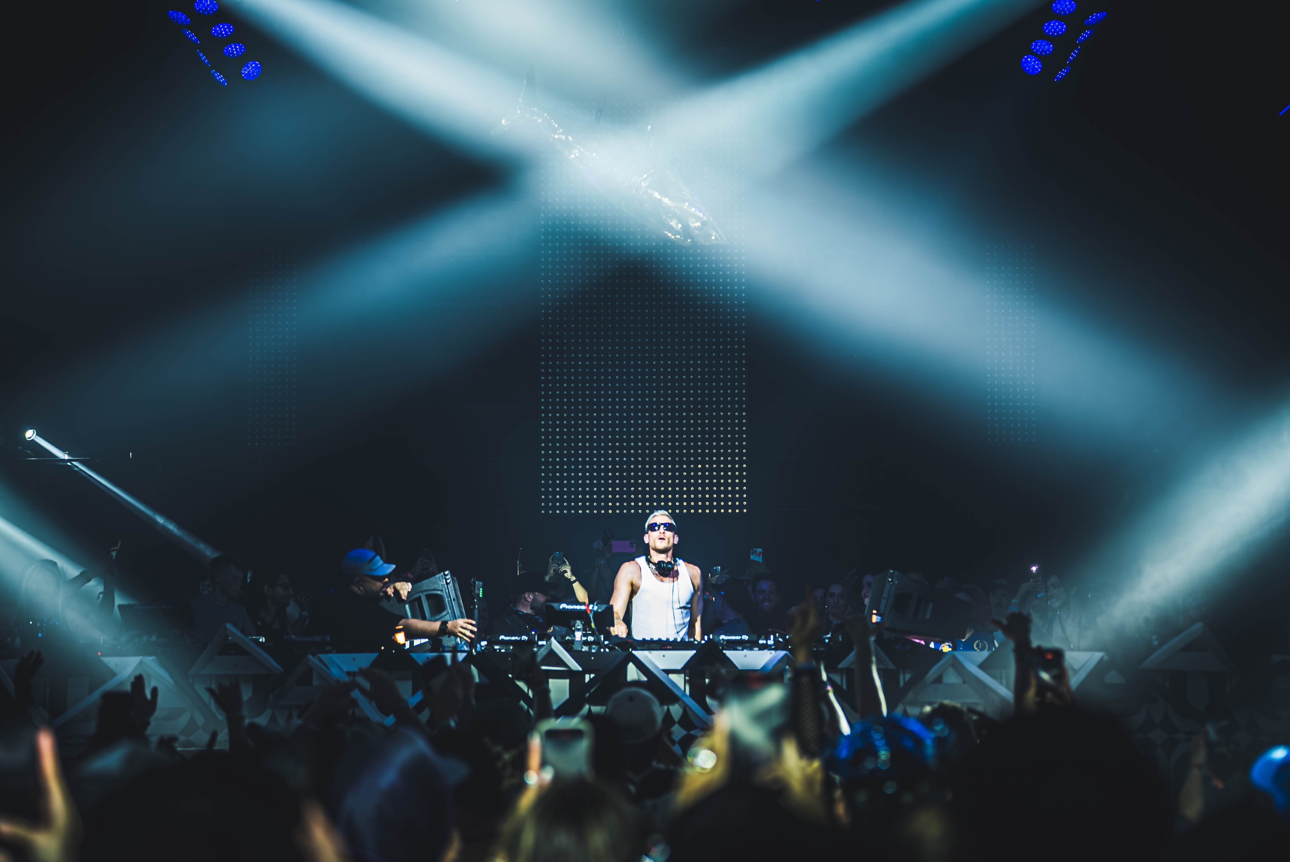 DJ performing on stage amidst vibrant lights and an enthusiastic crowd, creating a lively concert atmosphere