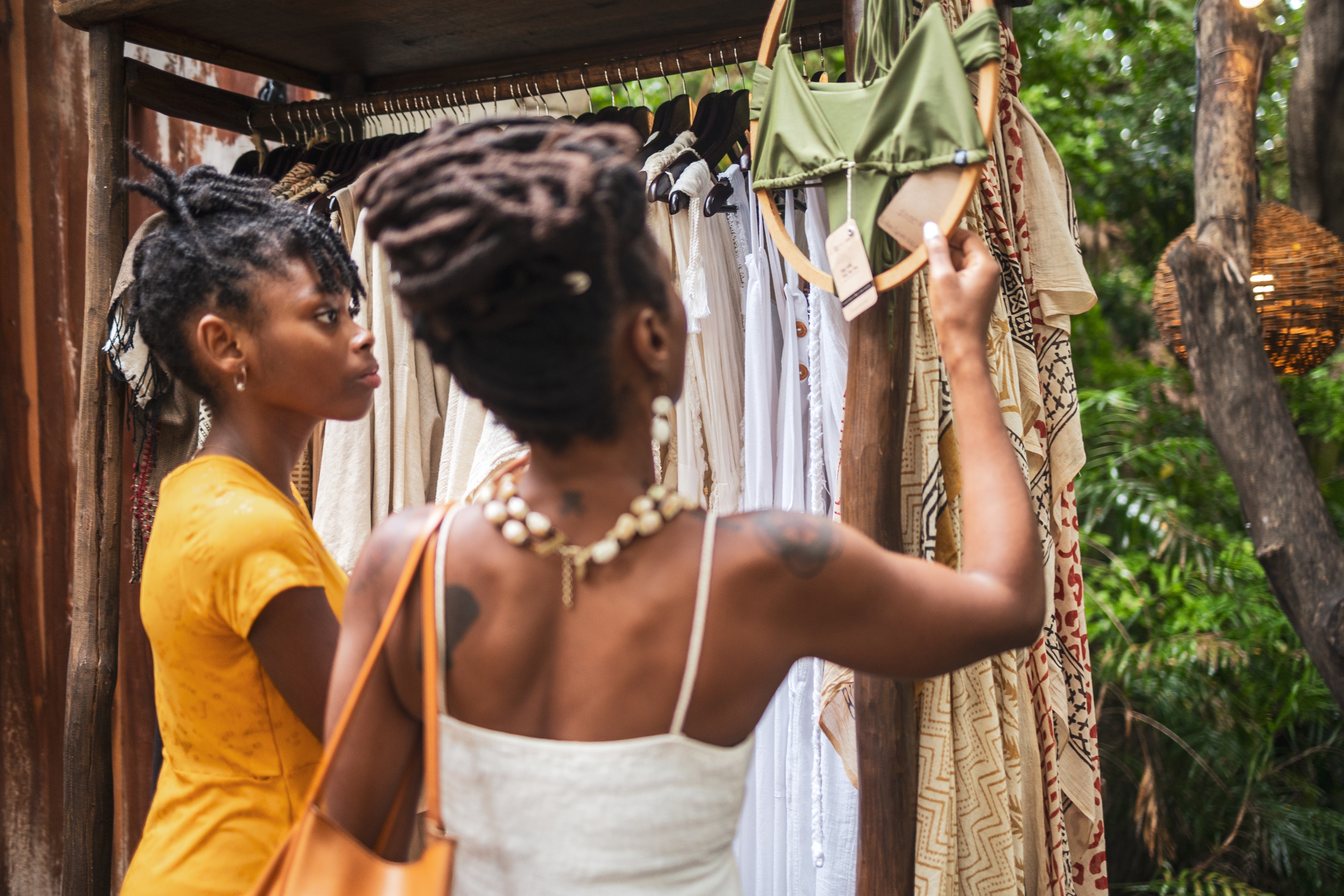 Two people browsing clothes on a rack outside; one holds up a green bikini top