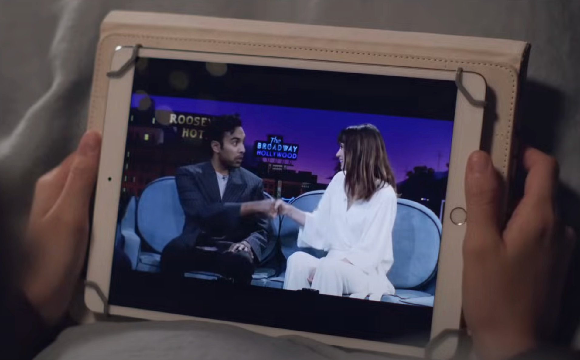Jack and Roxanne having a conversation on a talk show displayed on a tablet being held by a viewer