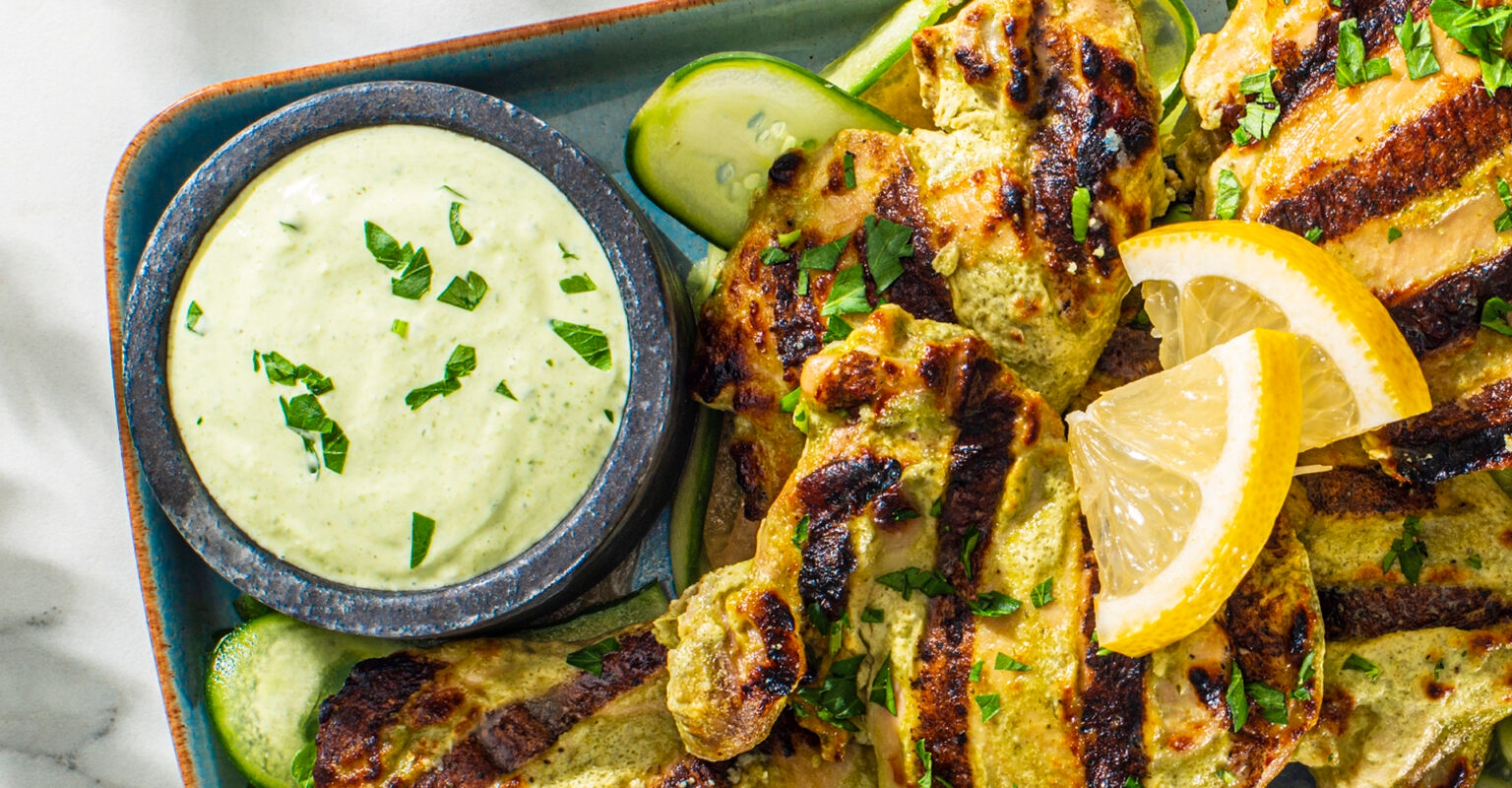 Grilled chicken drumsticks garnished with herbs and lemon slices, served with creamy herb dip and cucumber slices on a plate
