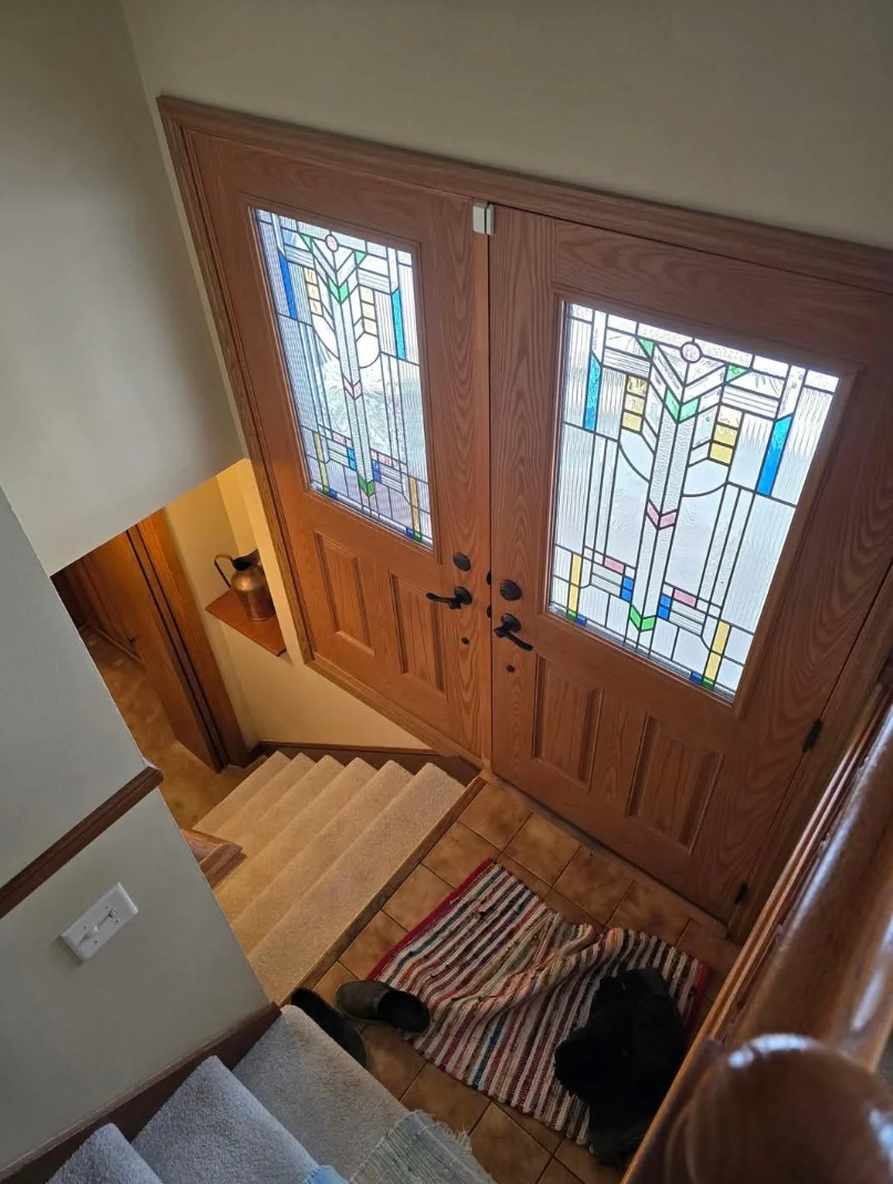 A home entry with wooden double doors featuring stained glass. A striped rug and a pair of shoes are on the floor near the carpeted stairs