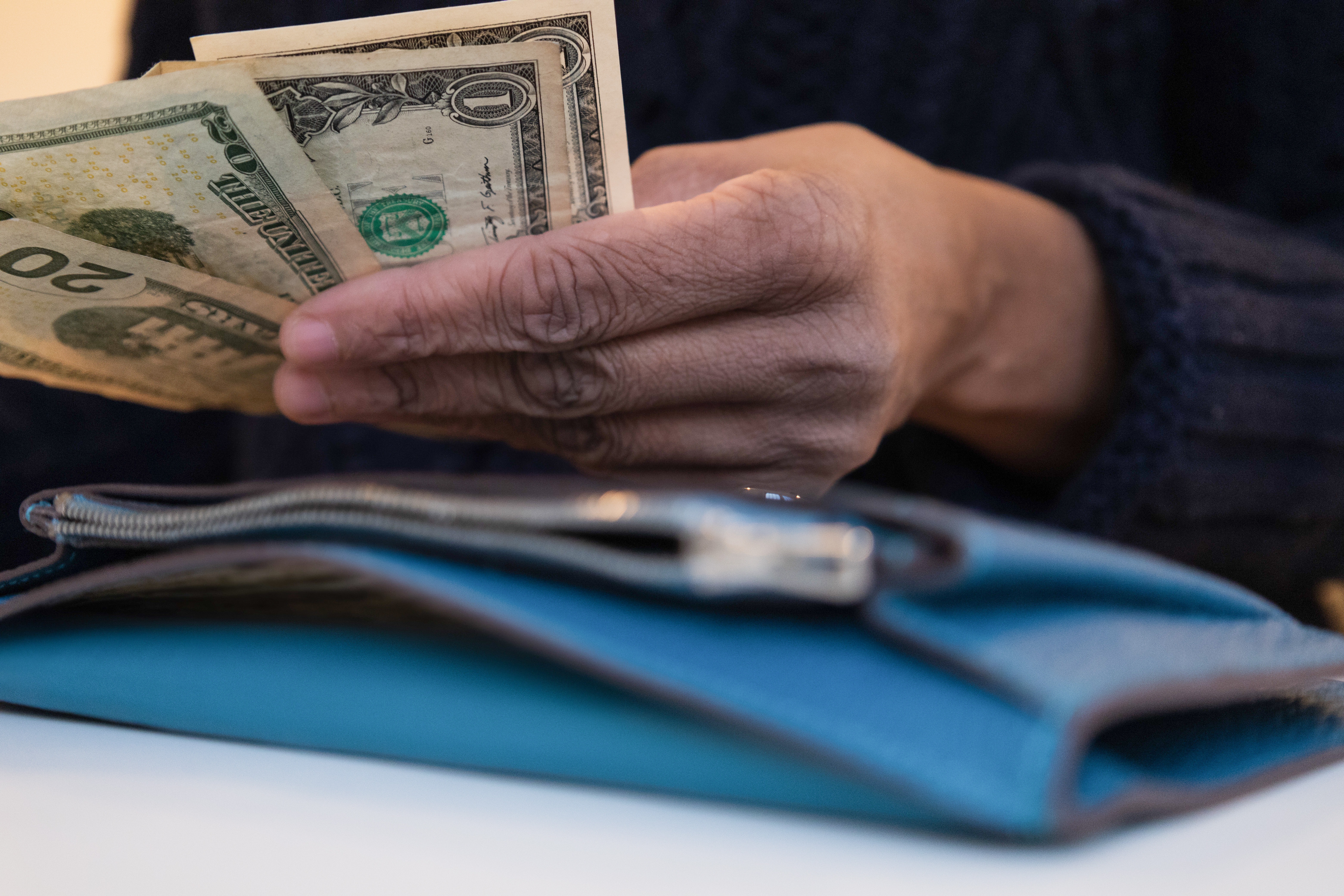 Person holding a few dollar bills, counting or organizing, with a wallet in the foreground