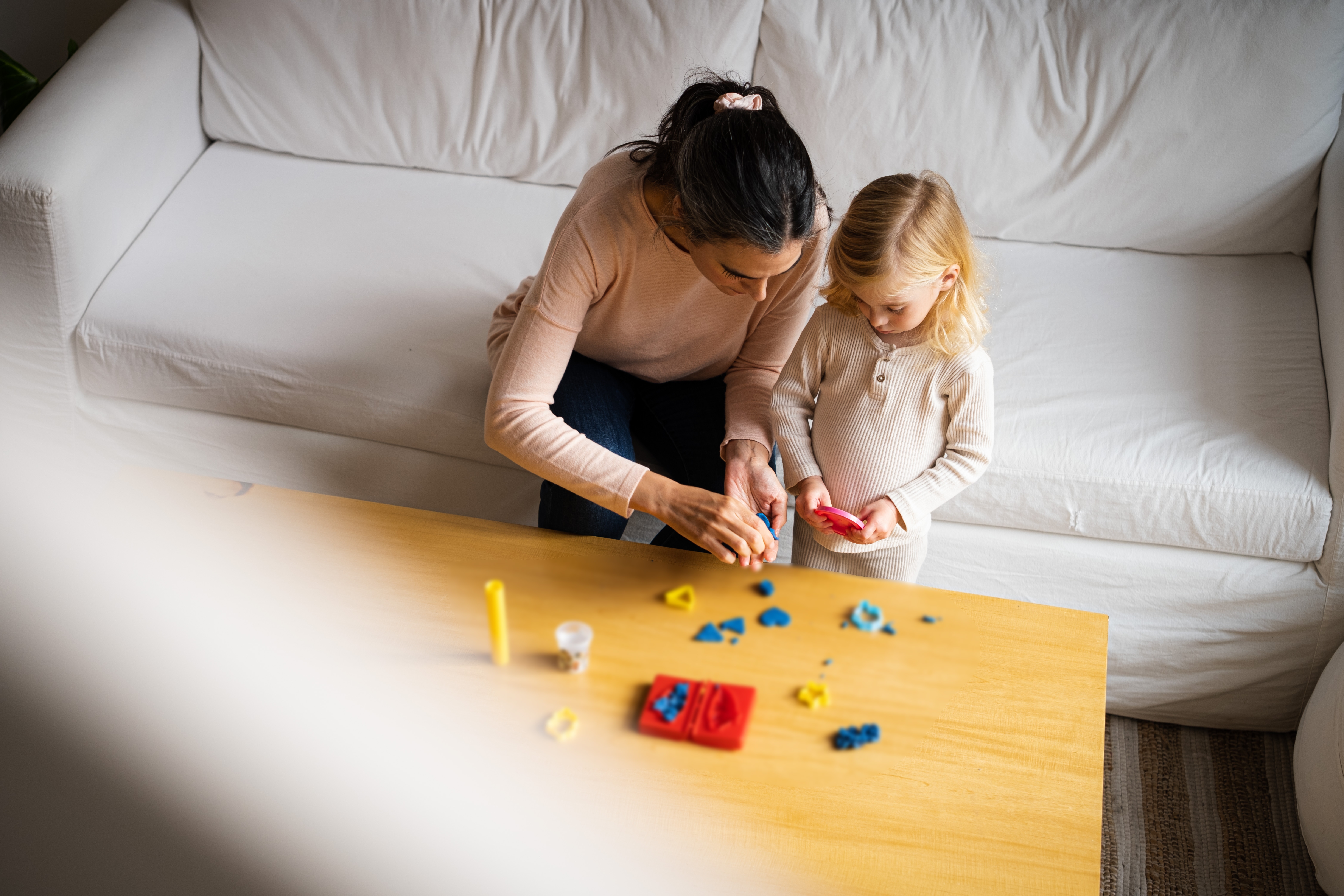 Woman and young child sitting on a sofa, playing with colorful clay on a wooden table