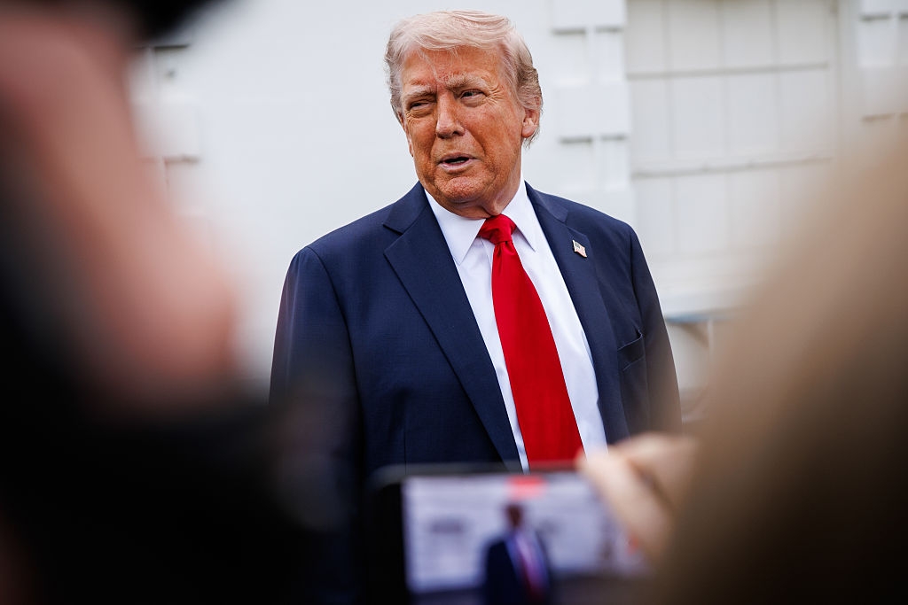 A person in a suit with a red tie is standing outside, surrounded by people taking photos