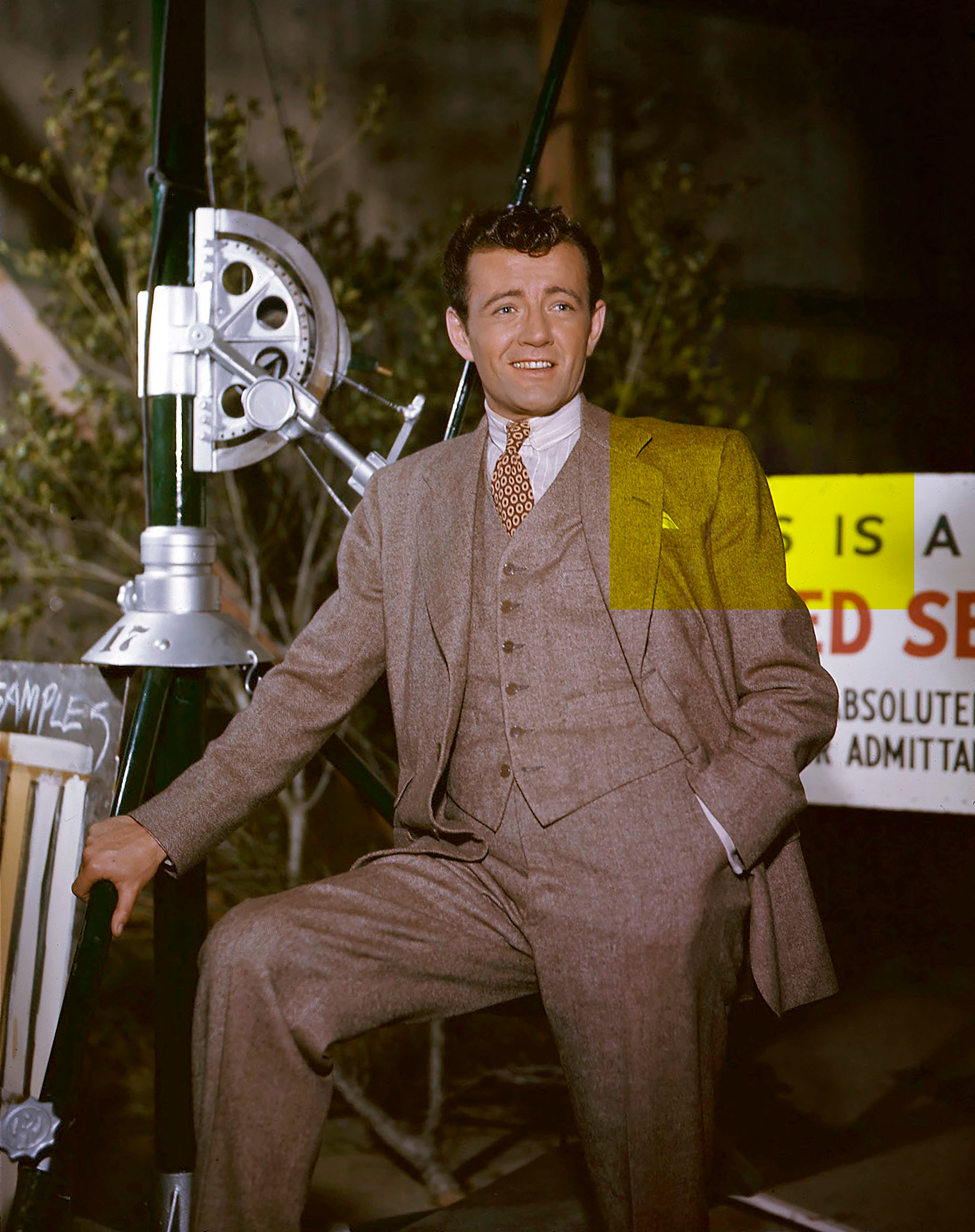 Man in a classic three-piece suit with a tie, posing outdoors beside equipment and signage